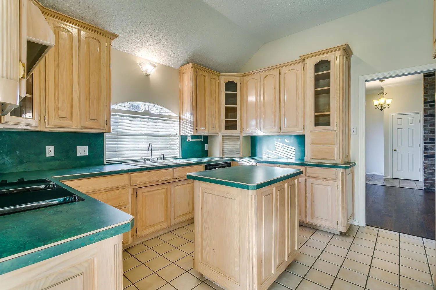 Kitchen featuring light wood-finish cabinetry, a central island, a built-in cooktop, and a window above the sink