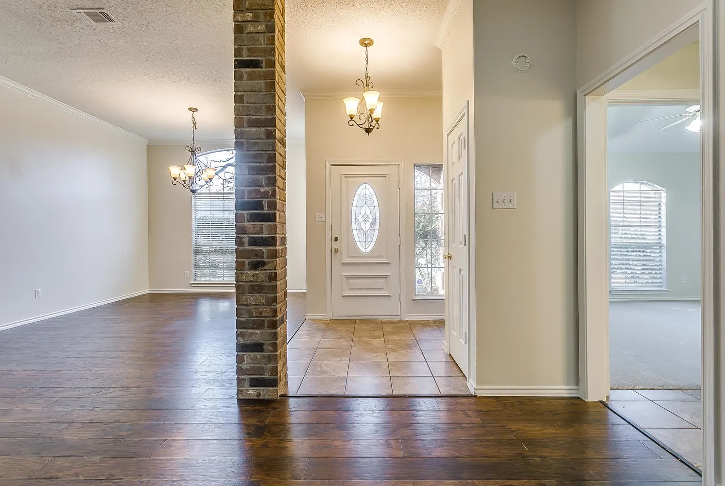 Wood-finish flooring, brick column accent, elegant front door with oval glass, decorative side windows, and a chandelier lighting fixture