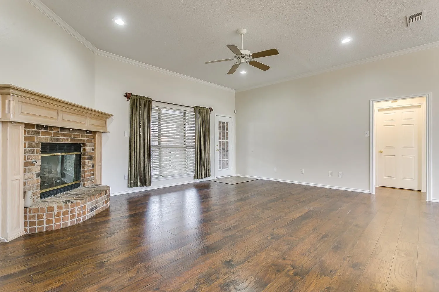 Brick fireplace with a wood mantel, wood-finish flooring, recessed lighting, ceiling fan, and French patio doors