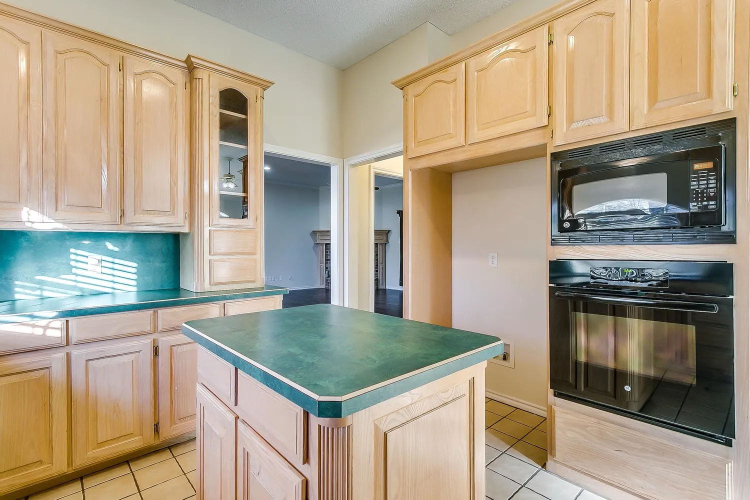 Kitchen featuring light wood cabinetry, a central island with a green countertop, matching green countertops, built-in oven, and a built-in microwave