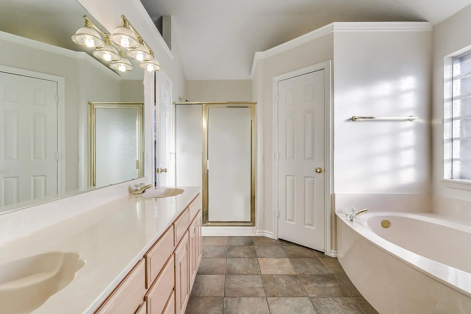 Spa-inspired primary bathroom featuring dual vanities with wood-finish cabinetry, marble countertops, and polished brass hardware