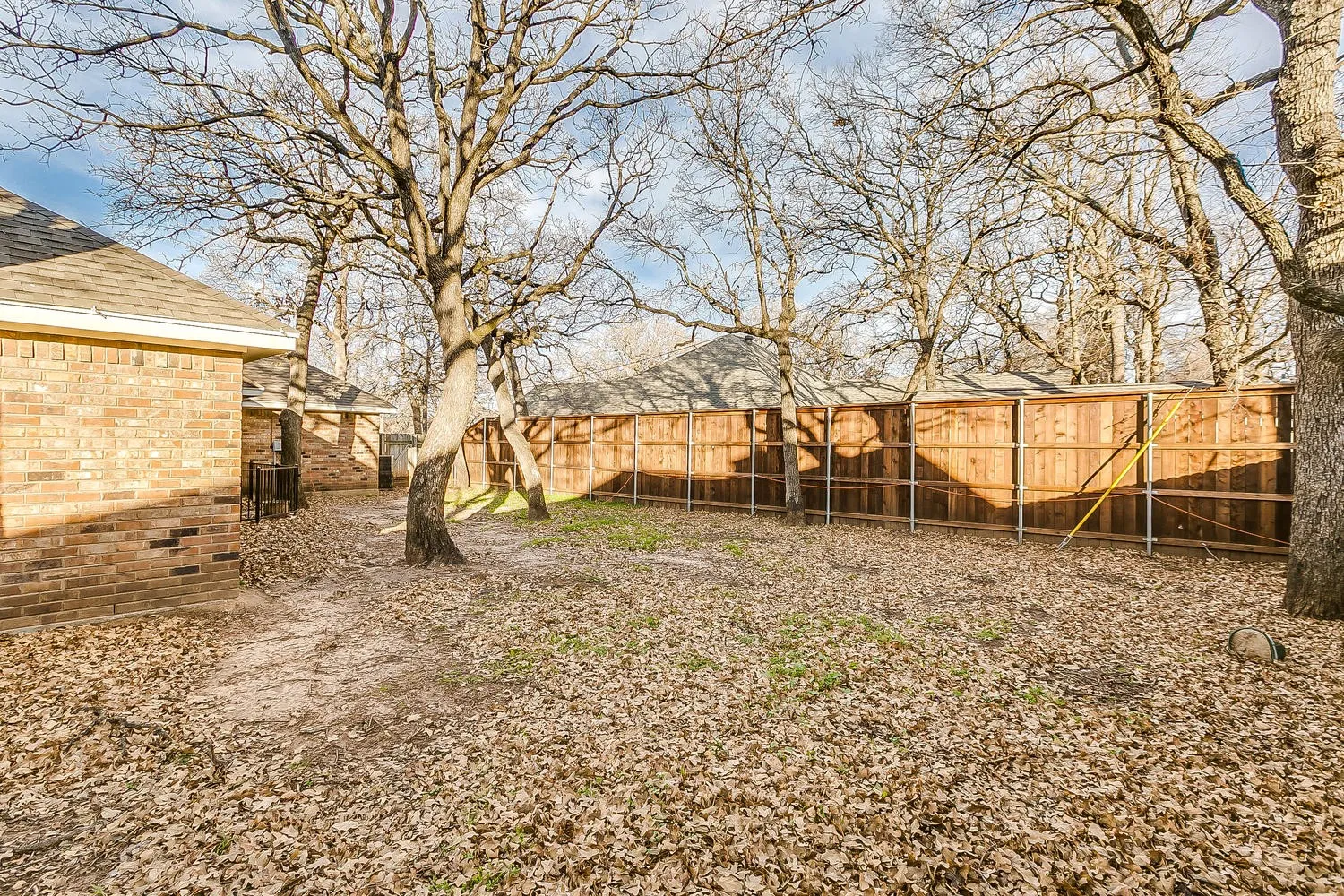 Spacious backyard with a wood-panel fence, mature trees, and a brick exterior