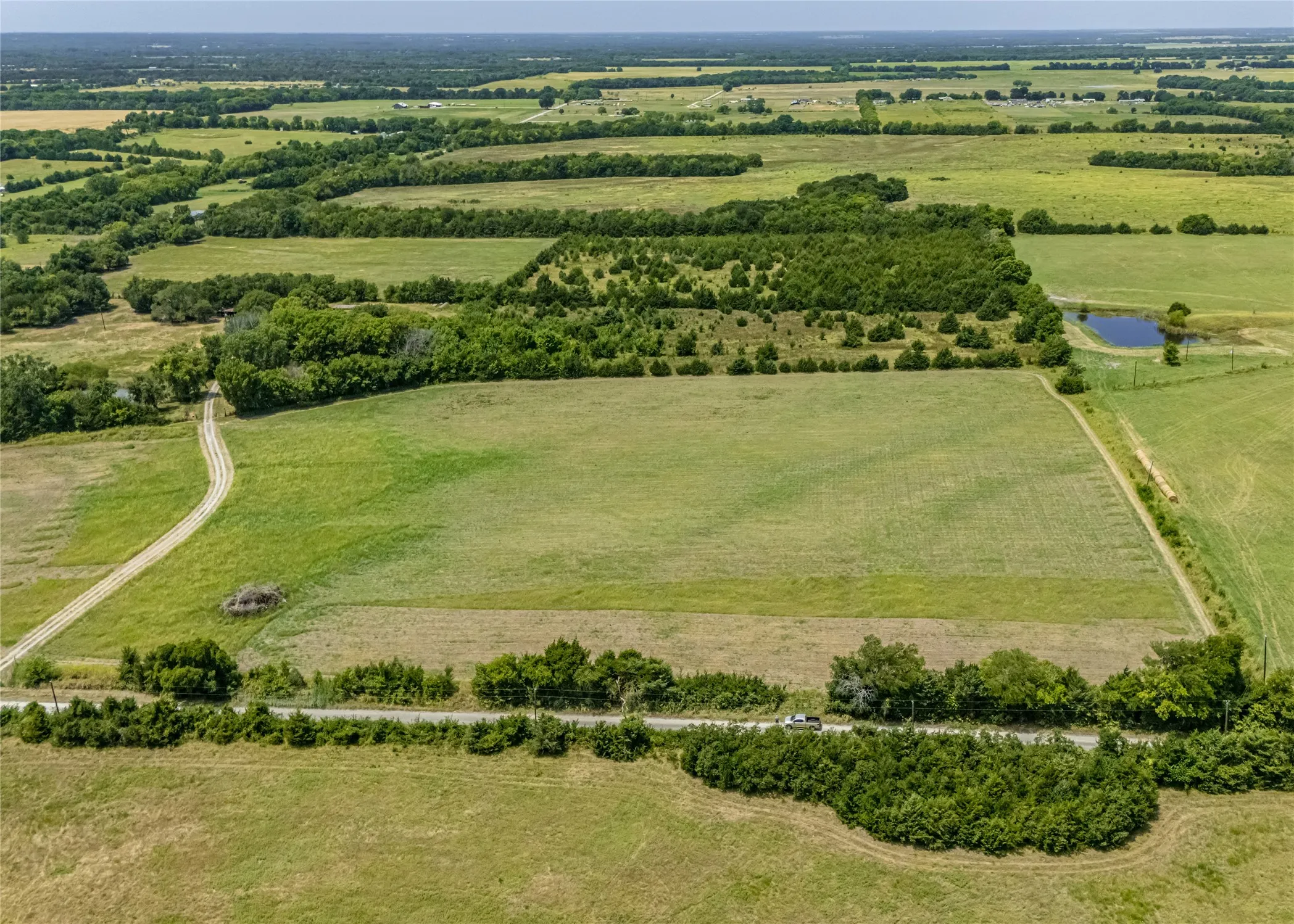 Expansive green fields with natural tree lines, a winding gravel road,