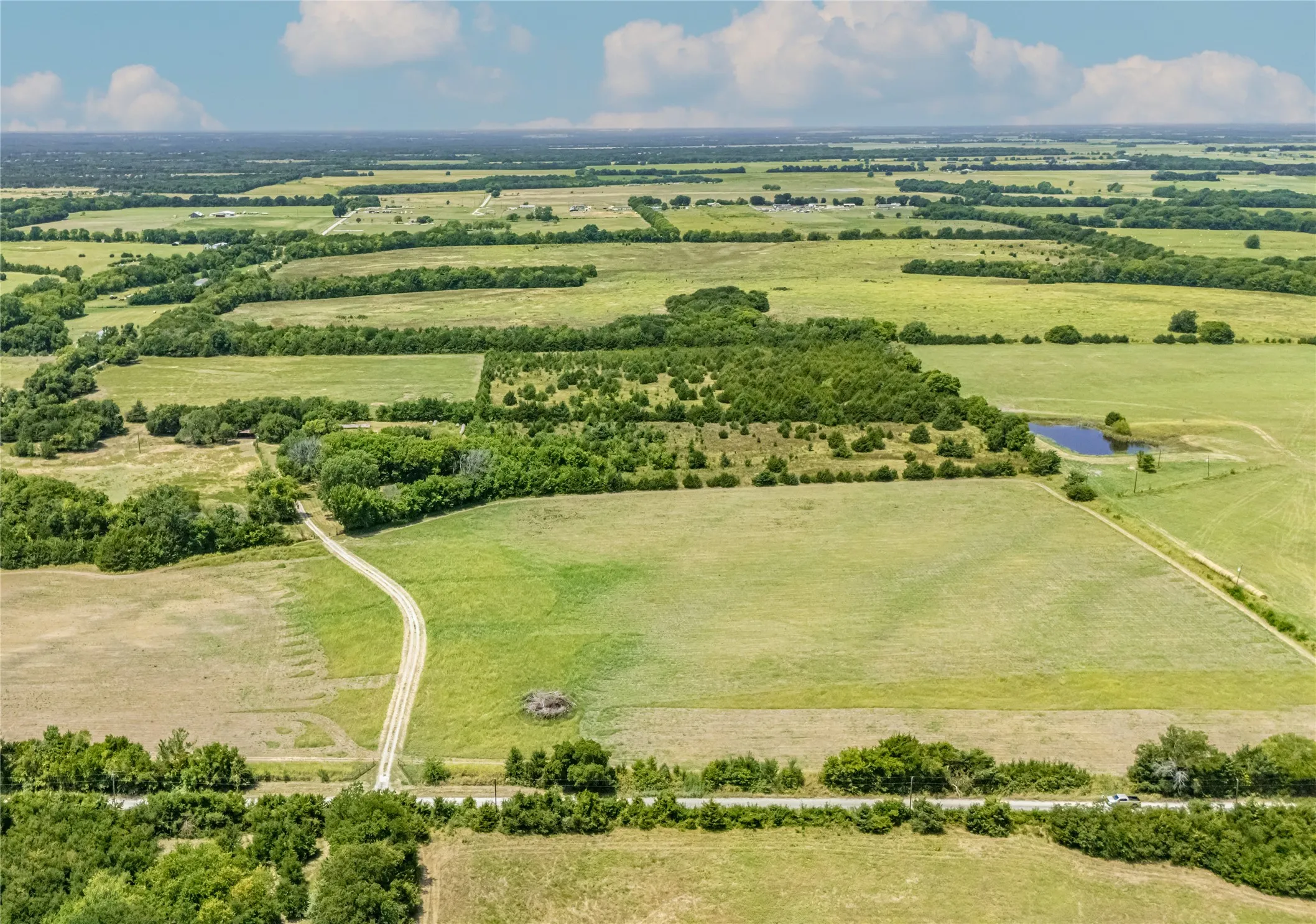 Expansive land parcel featuring open fields, scattered tree lines, and a visible pond