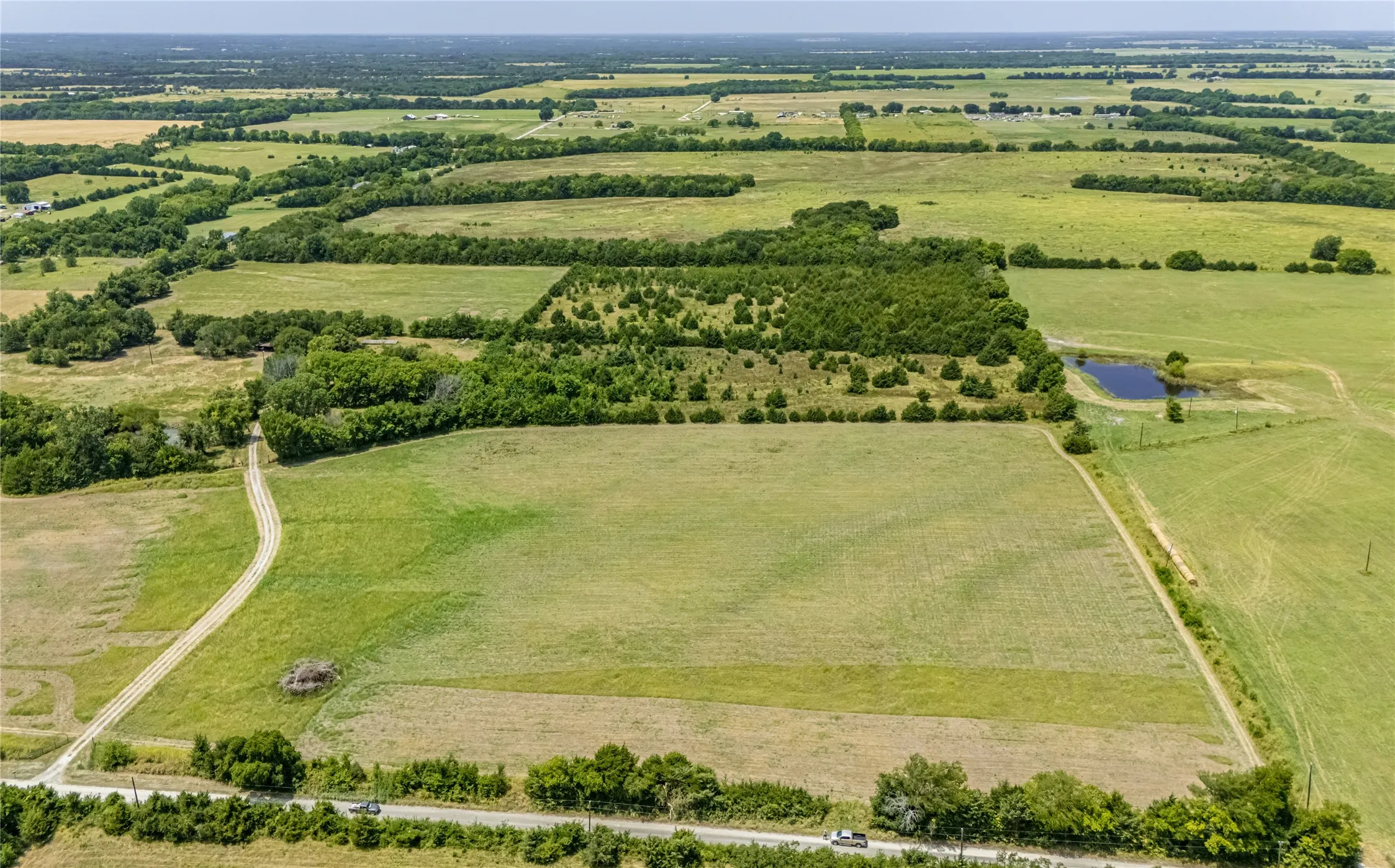 Expansive acreage featuring a hay field, mature trees, and a gravel road