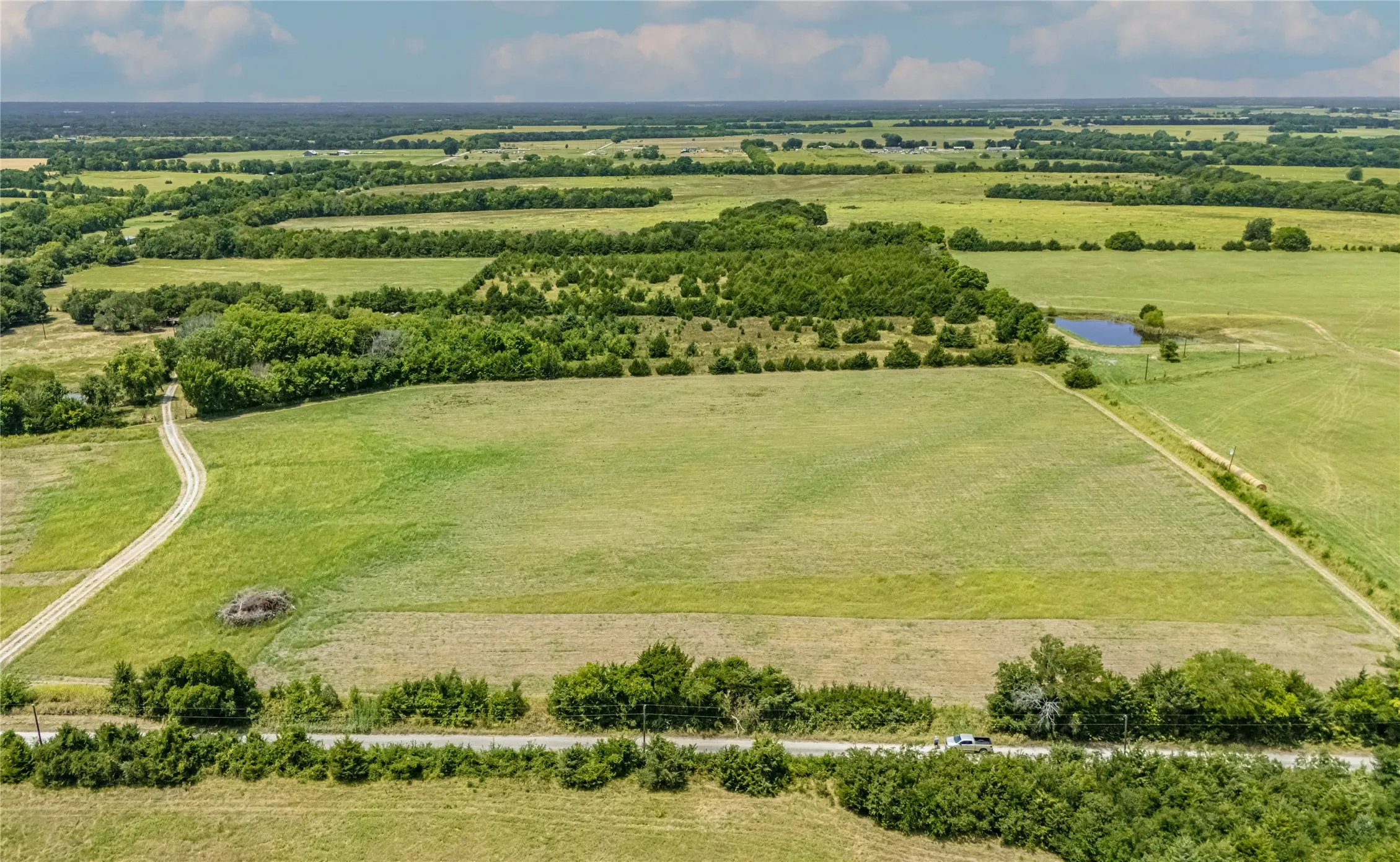 Expansive acreage, a gravel access road, and mature tree lines