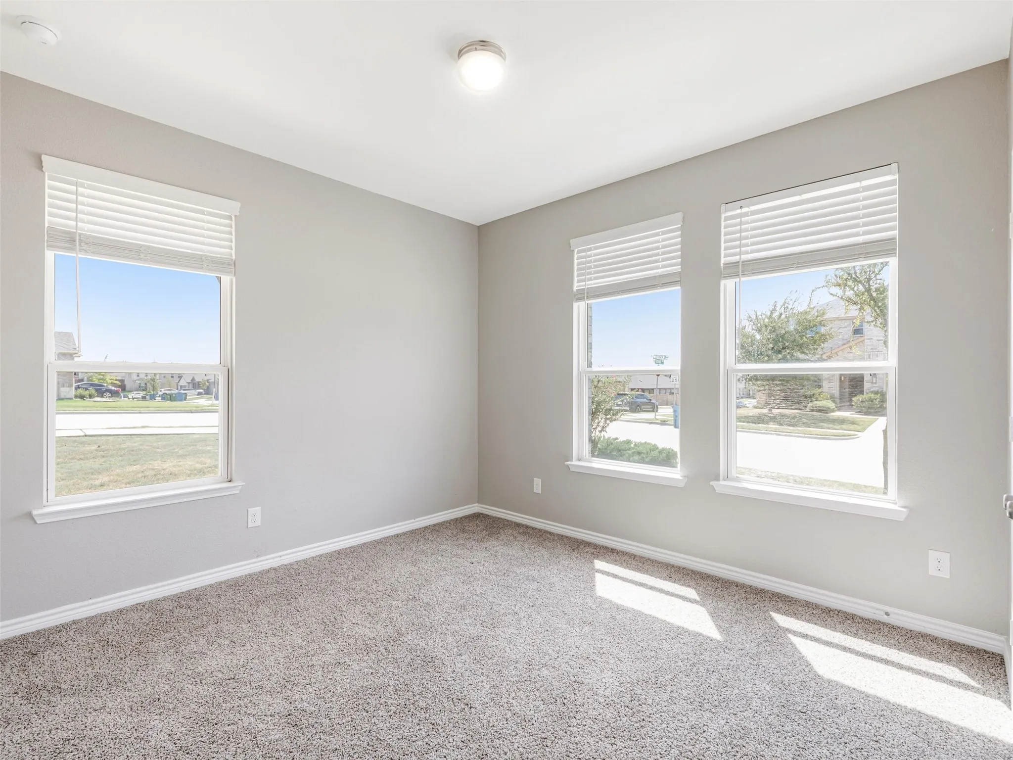 Bright secondary bedroom features three windows, abundant natural light, neutral finishes, and plenty of flexibility for guests, work, or hobbies.