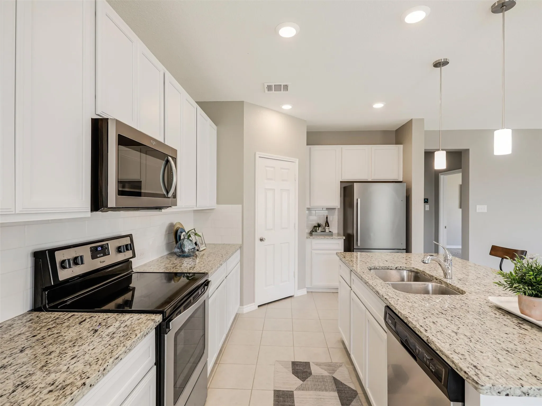 Kitchen offers granite countertops, a subway tile backsplash, stainless steel appliances, generous cabinet storage, and a large center island with a double sink.
