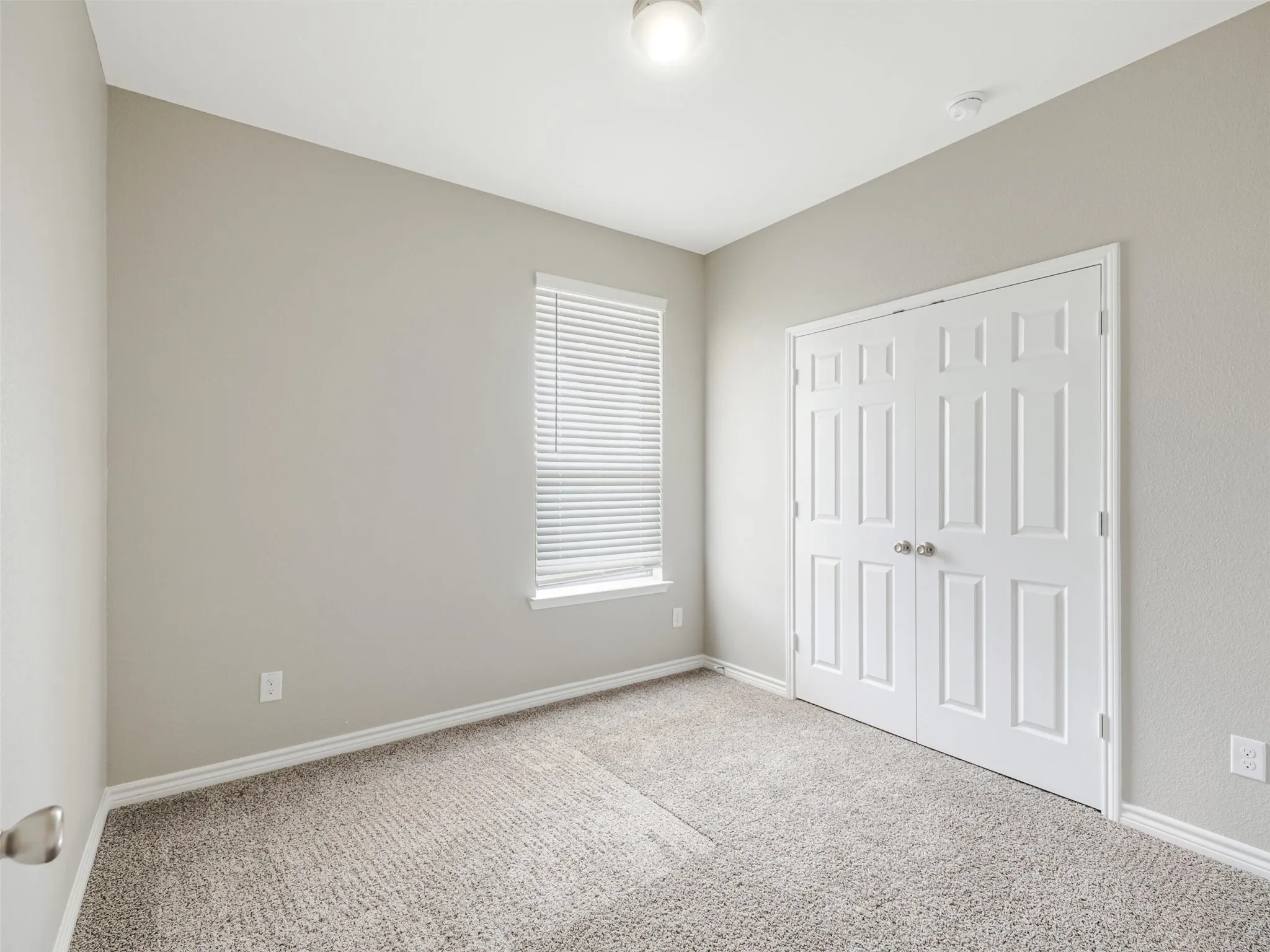 Secondary bedroom includes neutral finishes, comfortable carpeting, natural light, and a wide closet with double doors.
