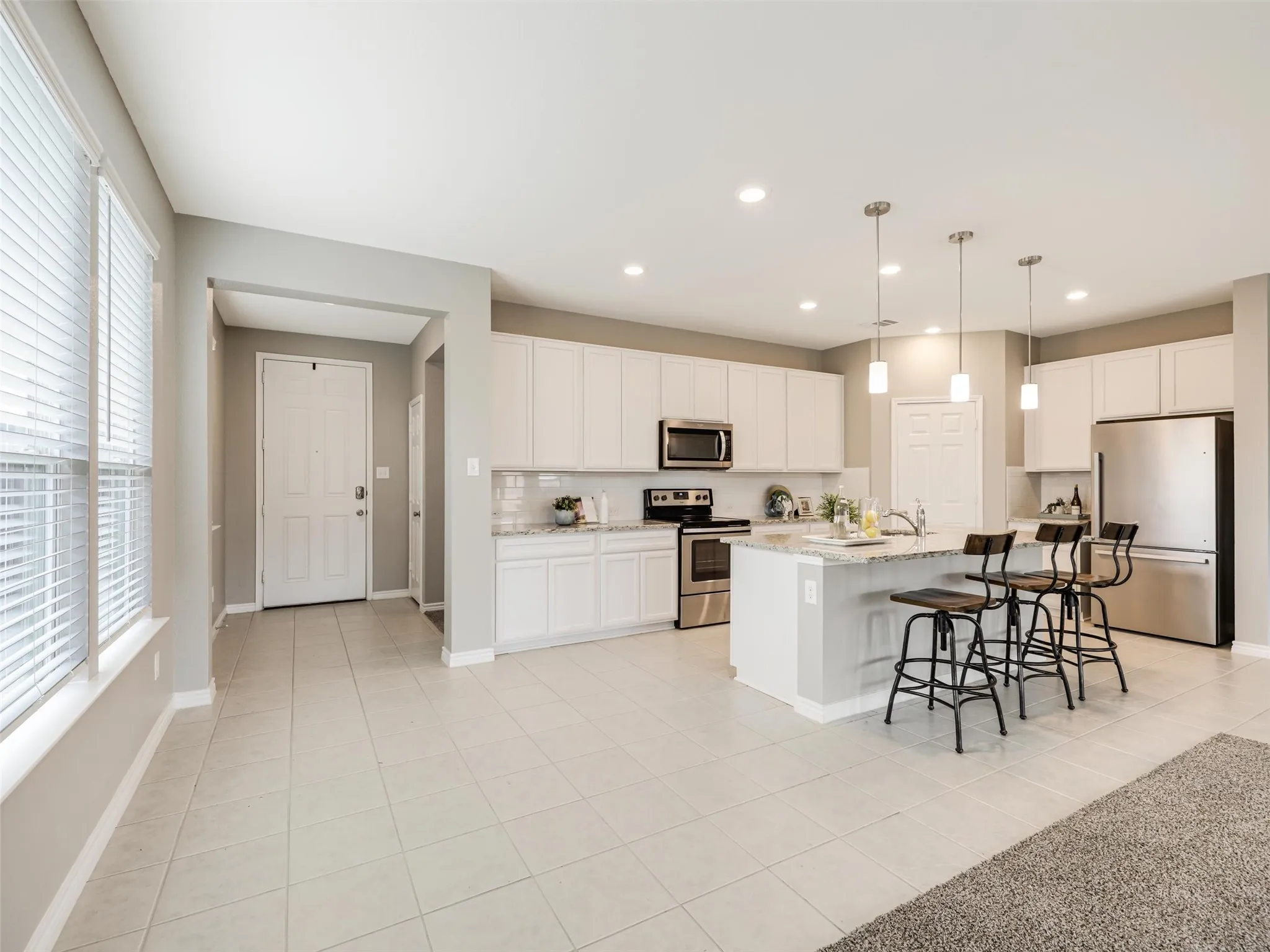 Bright, spacious kitchen with white cabinetry, granite countertops, stainless steel appliances, modern pendant lighting, and an oversized island with bar seating.