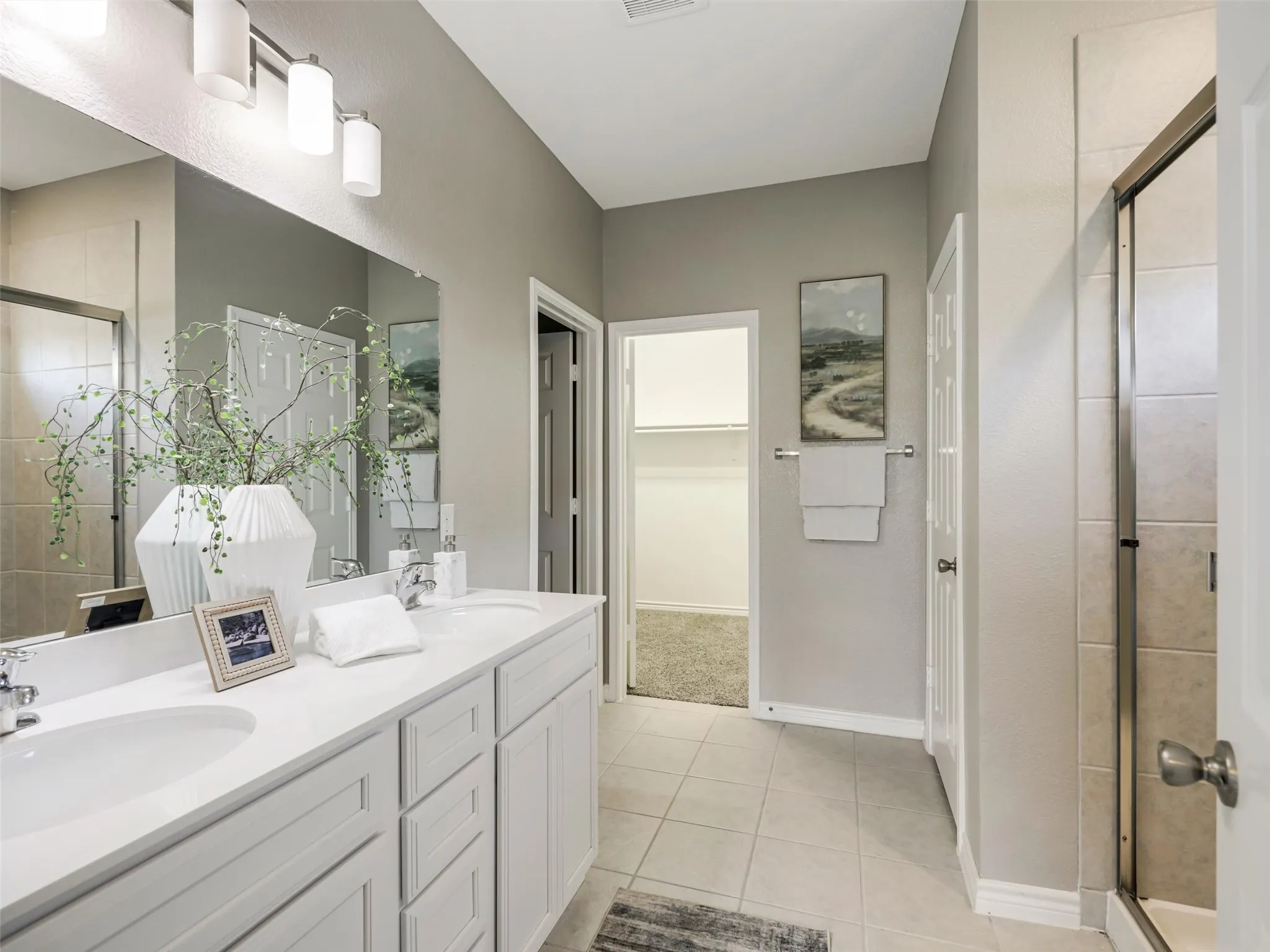 Private primary bathroom features a dual-sink vanity, expansive mirror, modern lighting, separate tiled shower, and direct access to the walk-in closet.