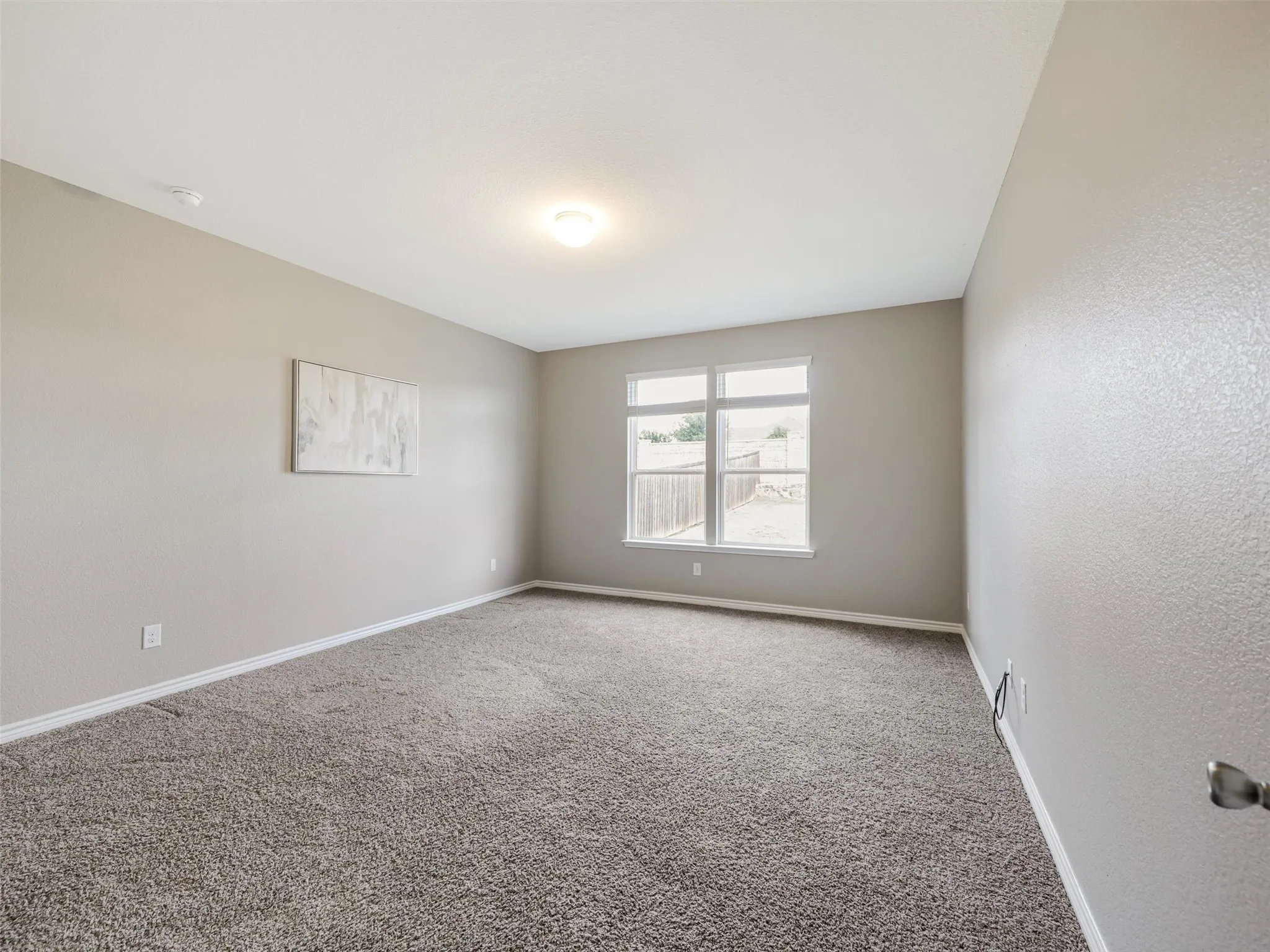 Spacious primary bedroom features neutral finishes, plush carpeting, and large windows overlooking the backyard.