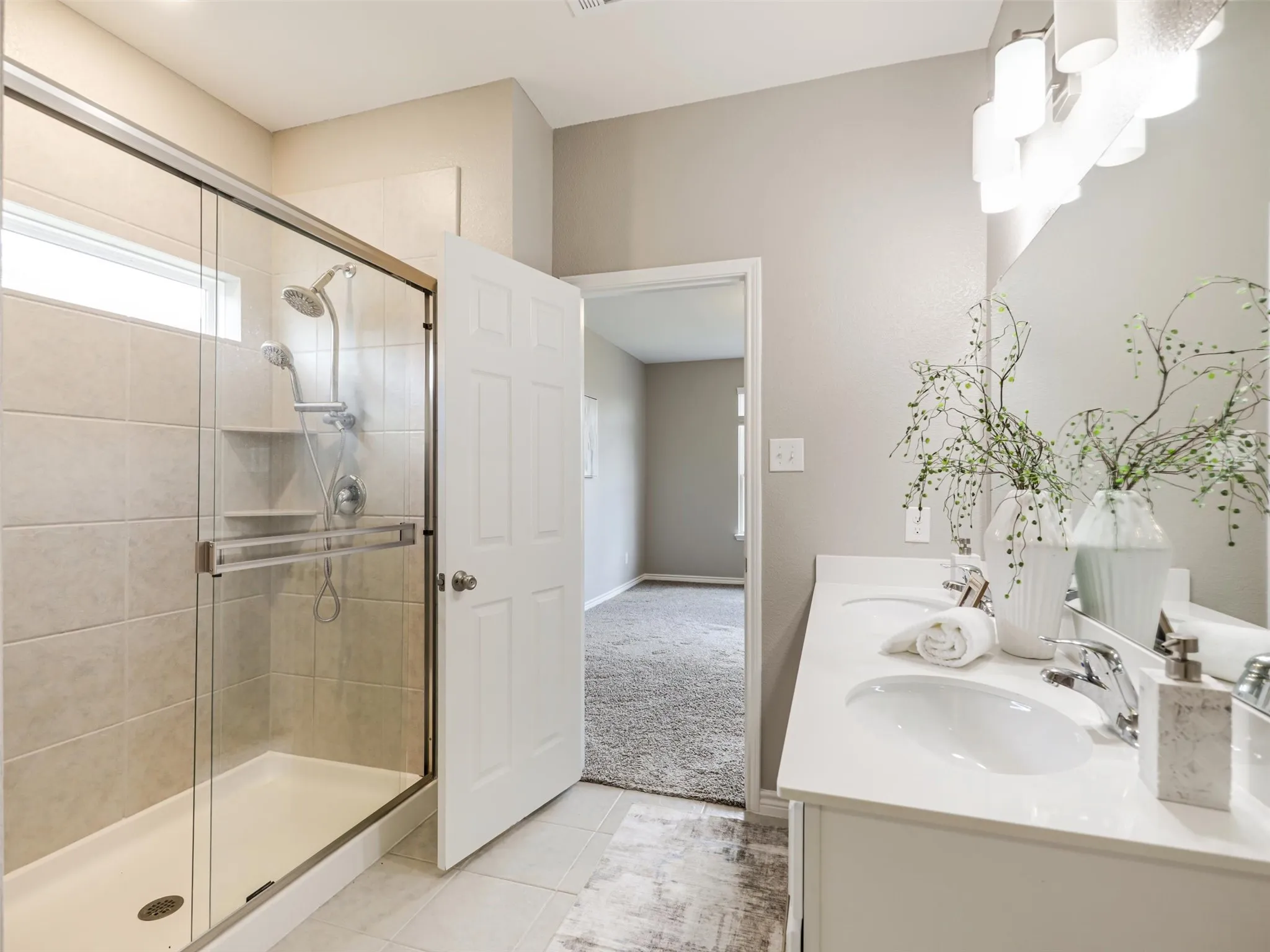 Primary bathroom features a dual-sink vanity, expansive mirror, modern lighting, and a separate tiled shower with a glass enclosure and multiple showerheads.