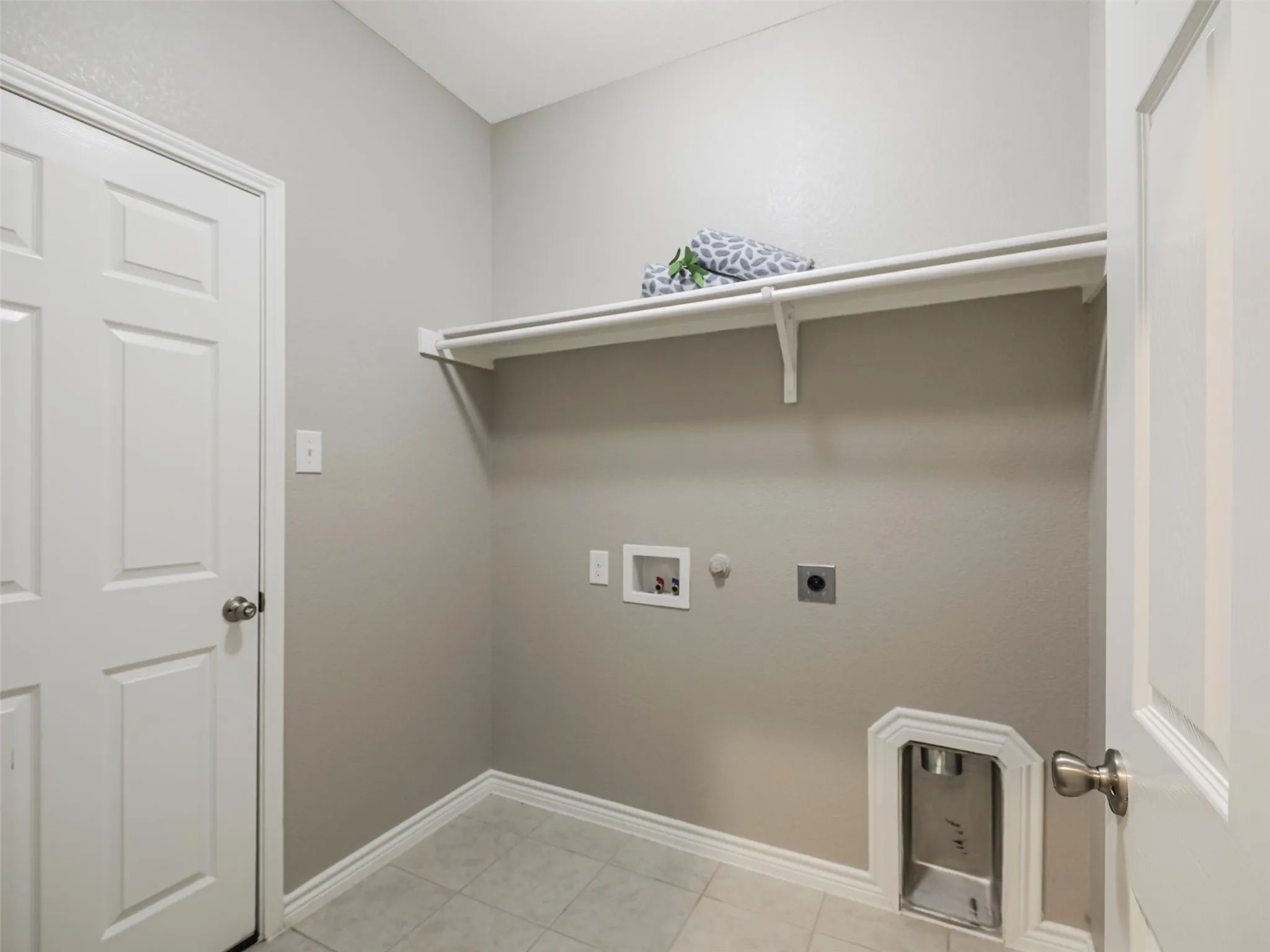 Dedicated laundry room offers washer and dryer connections, built-in shelving, tile flooring, and additional storage space.