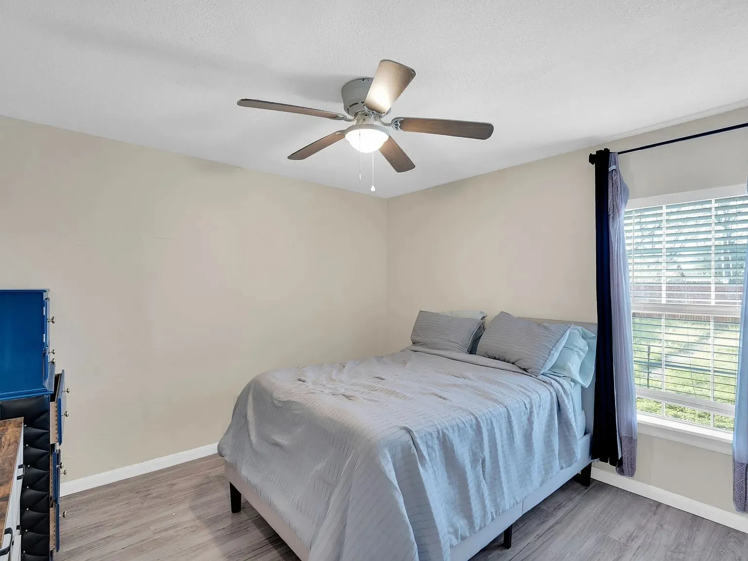 Bright secondary bedroom featuring wood-finish flooring, neutral wall finishes, and abundant natural light from a large window with plantation shutters