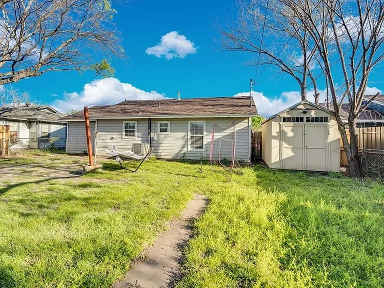 Rear property exterior with a detached storage shed, a paved pathway, and mature trees