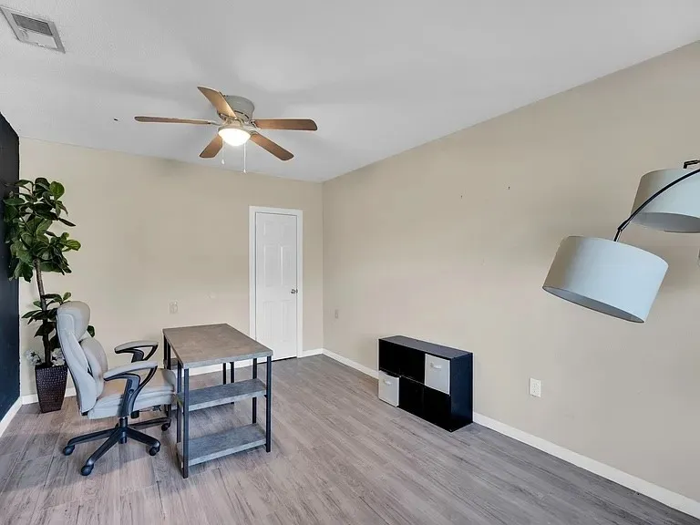 Wood-finish flooring, ceiling fan with light fixture, four-panel interior door, and neutral wall paint