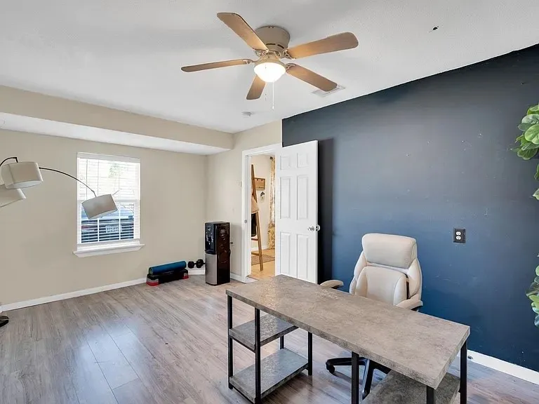 Wood-finish flooring, ceiling fan with integrated lighting, window with blinds, and a paneled interior door