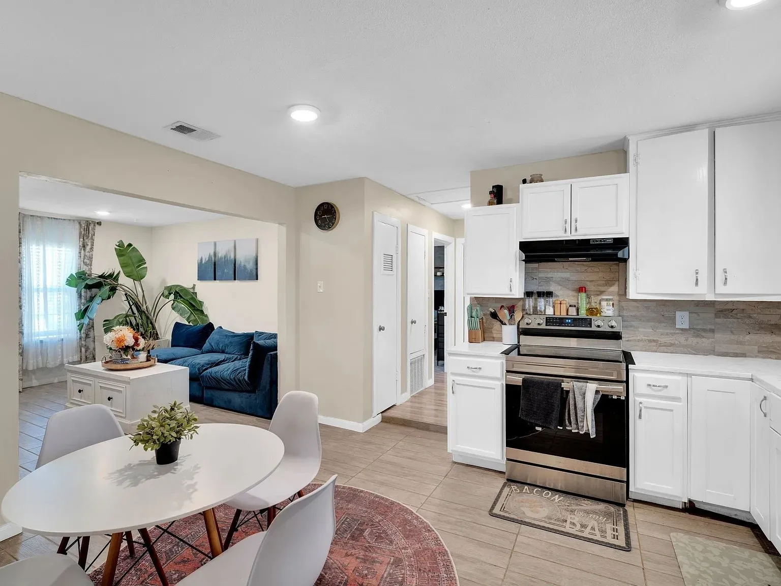 Open-concept kitchen and dining area featuring white cabinetry, tile backsplash, and stainless steel appliances