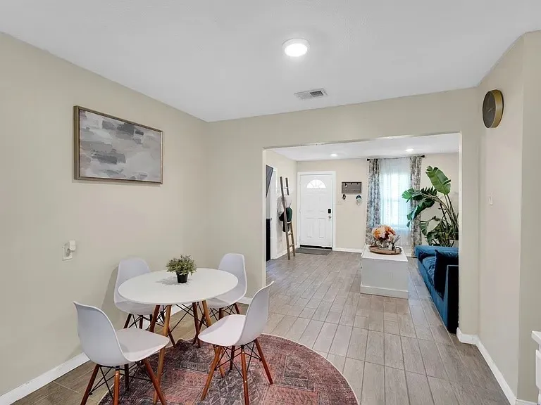 Bright, open-concept dining area featuring a round table with wood-finish base, white modern chairs, and warm neutral walls
