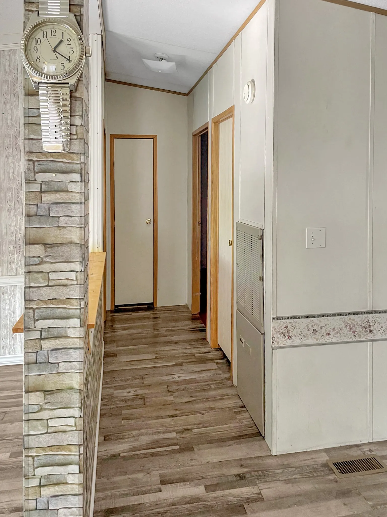 Hallway featuring wood-finish flooring, stone accent wall with integrated clock, and multiple door openings with natural wood frames