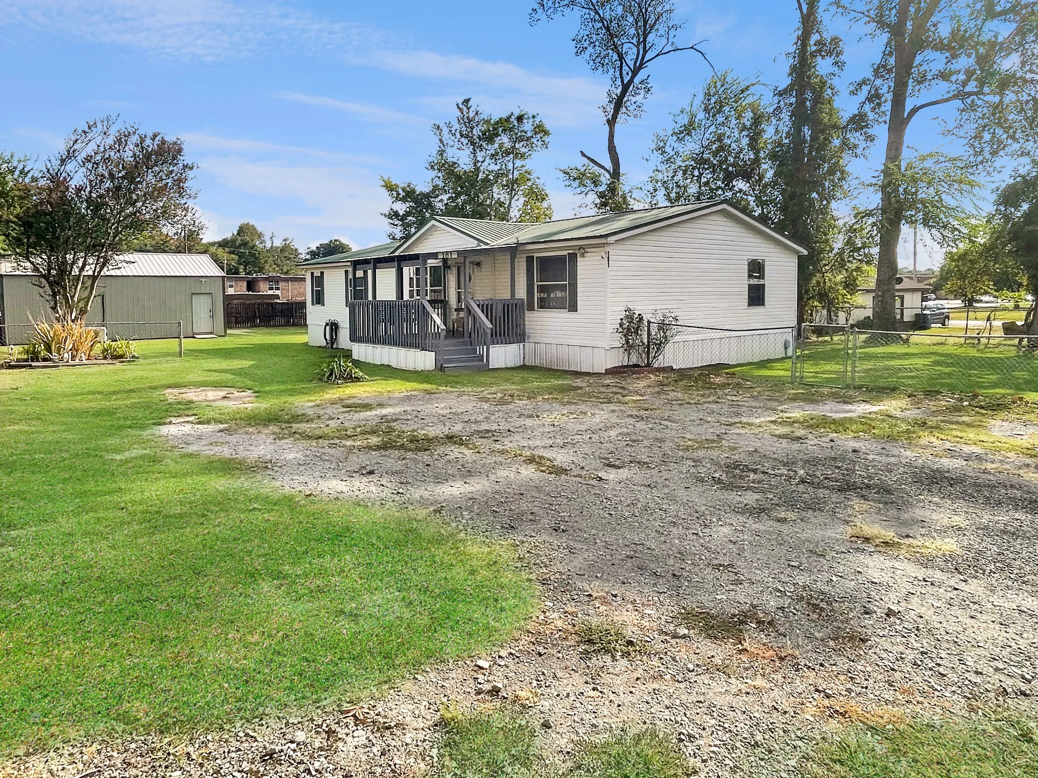 Charming manufactured home situated on expansive grounds featuring a manicured lawn, mature landscaping, and detached garage