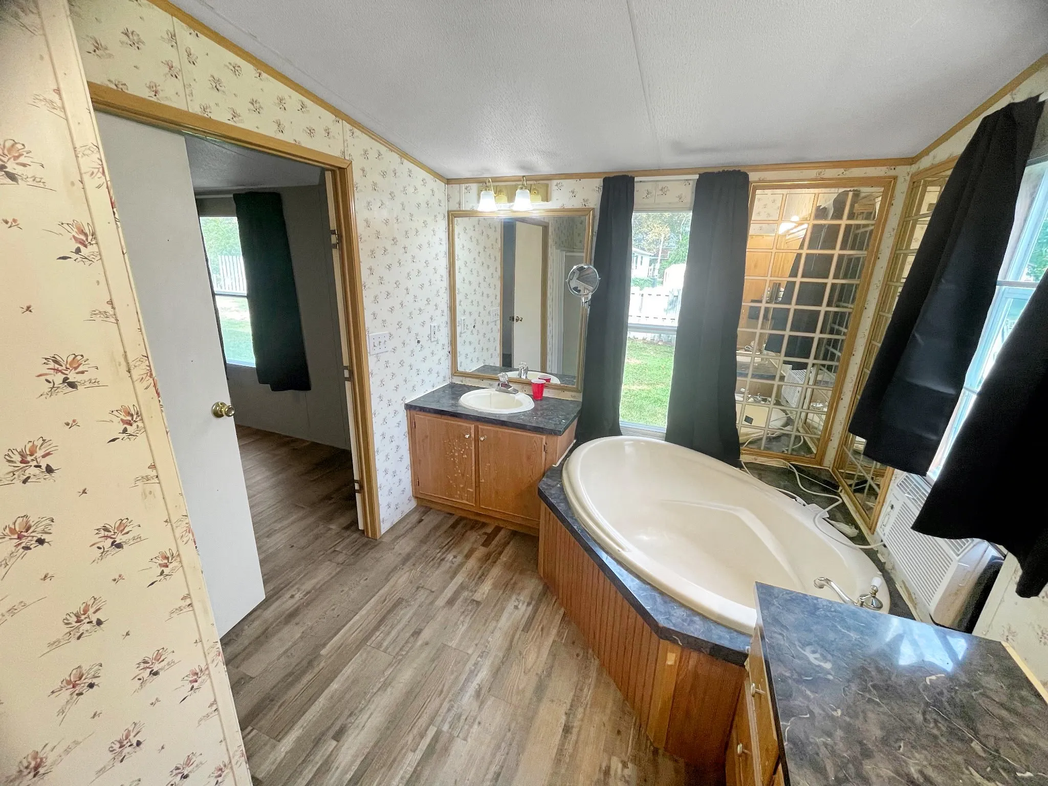 Spa-inspired primary bathroom featuring a freestanding soaking tub with wood-finish paneling, dual vanity with ample storage, wood-finish flooring throughout, and abundant natural light from multiple windows