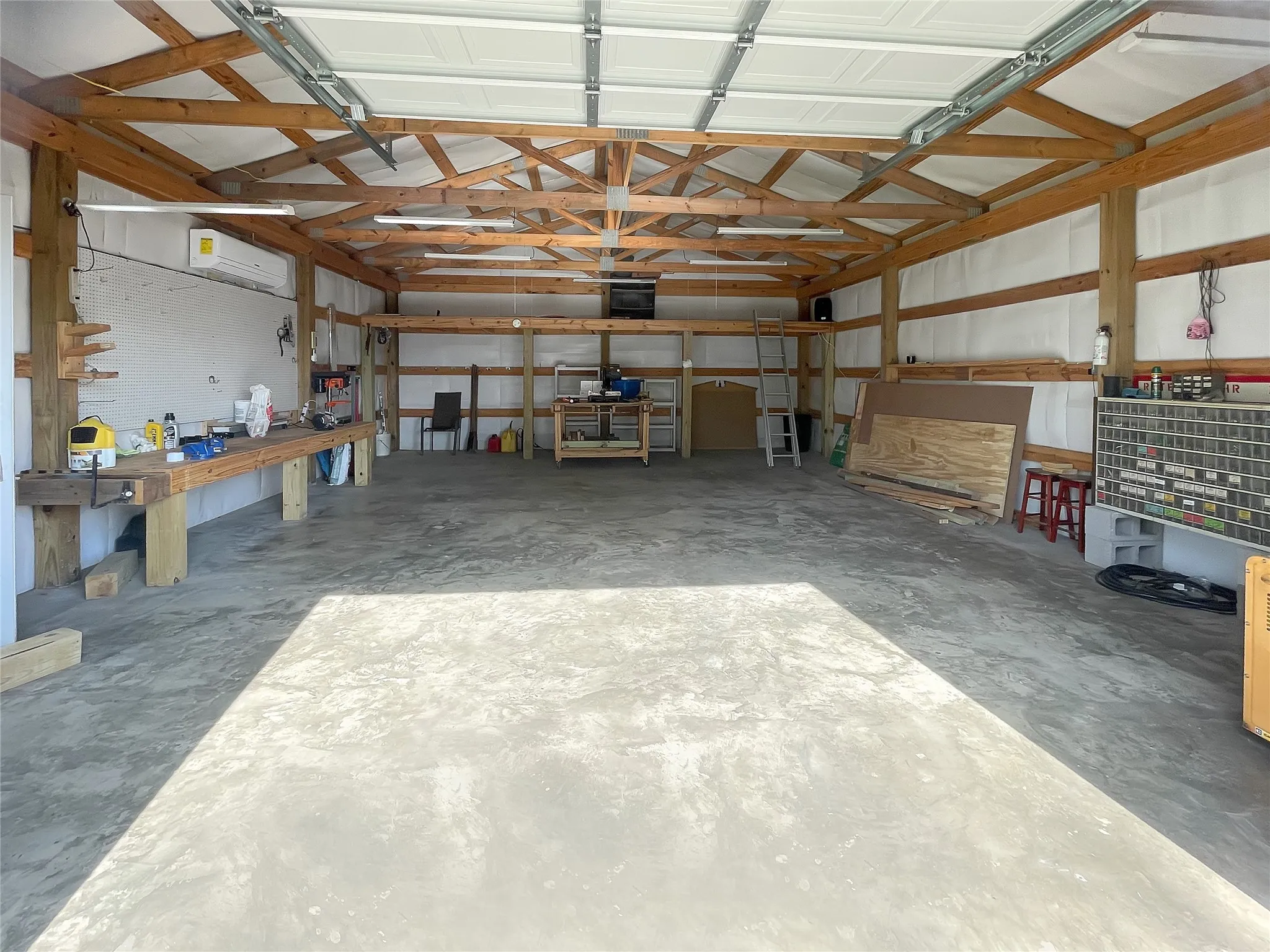 Spacious workshop featuring exposed wood-beam ceiling with skylights, polished concrete flooring, built-in work surfaces along the perimeter, and ample overhead storage