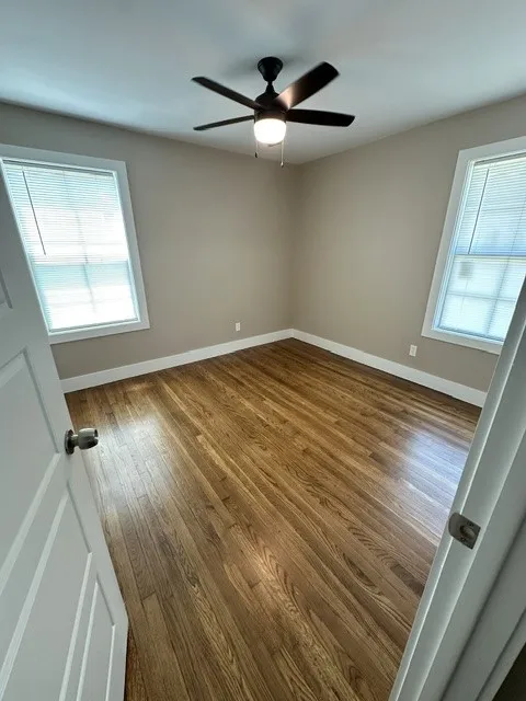 Hardwood flooring, neutral wall tones, two windows with blinds, and a ceiling fan with integrated lighting