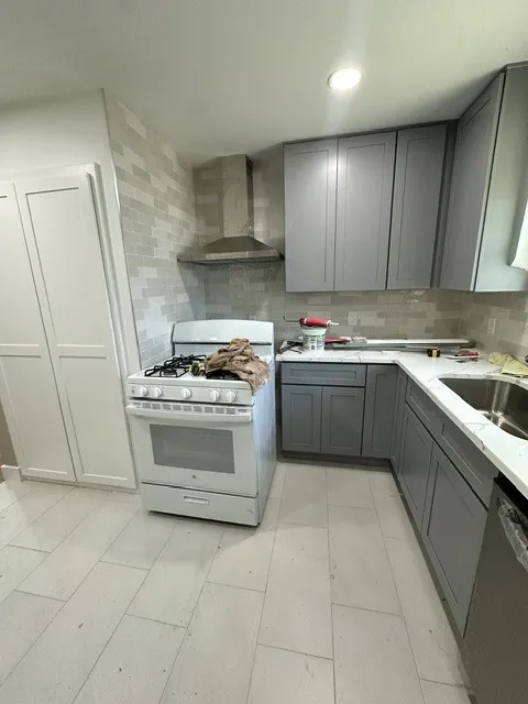Modern kitchen featuring stainless steel gas range and hood ventilation, soft-close cabinetry with gray finish, quartz countertops, subway tile backsplash, and tile flooring throughout