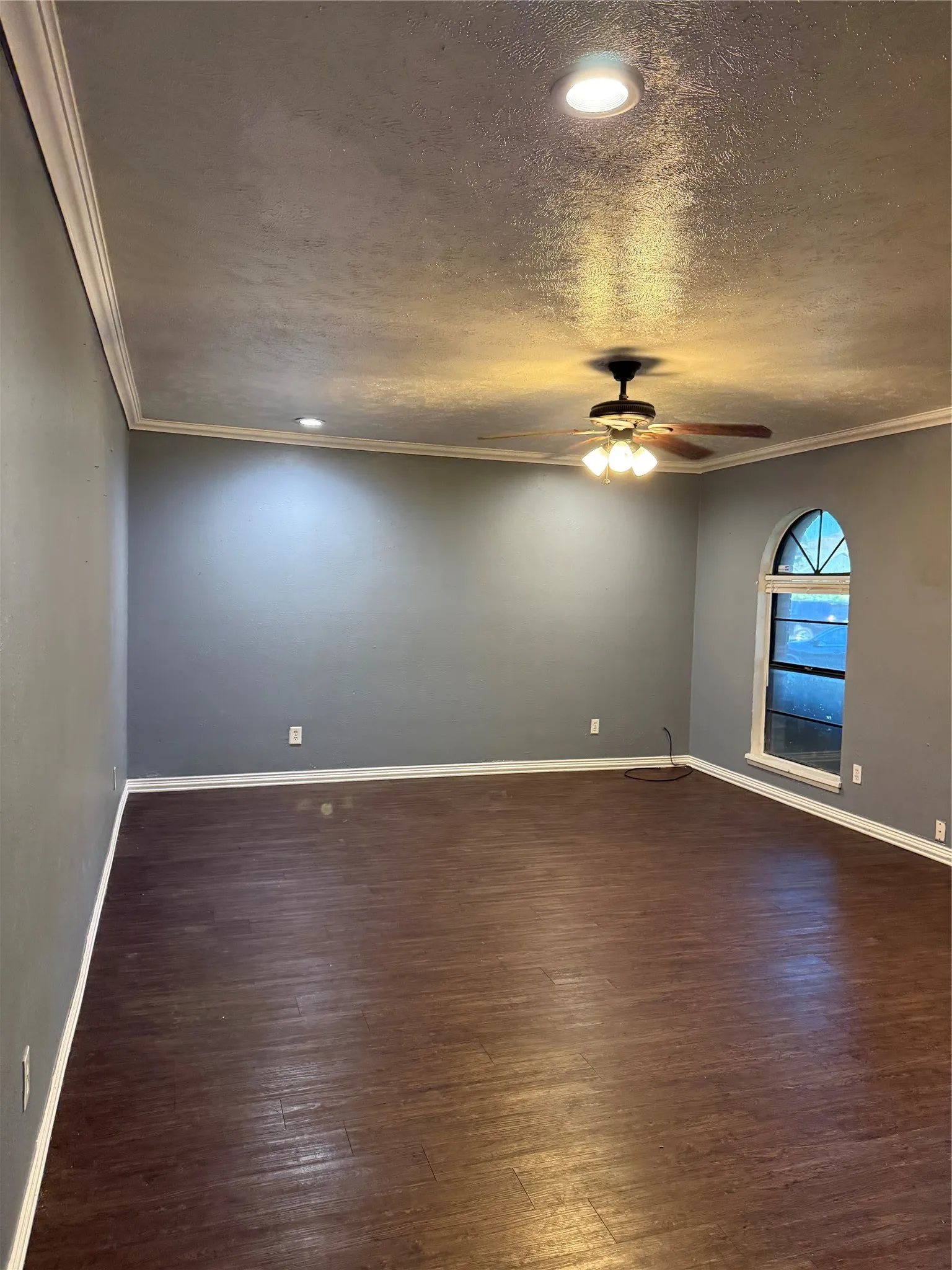 Wood-finish flooring, recessed lighting, crown molding, ceiling fan, and arched window