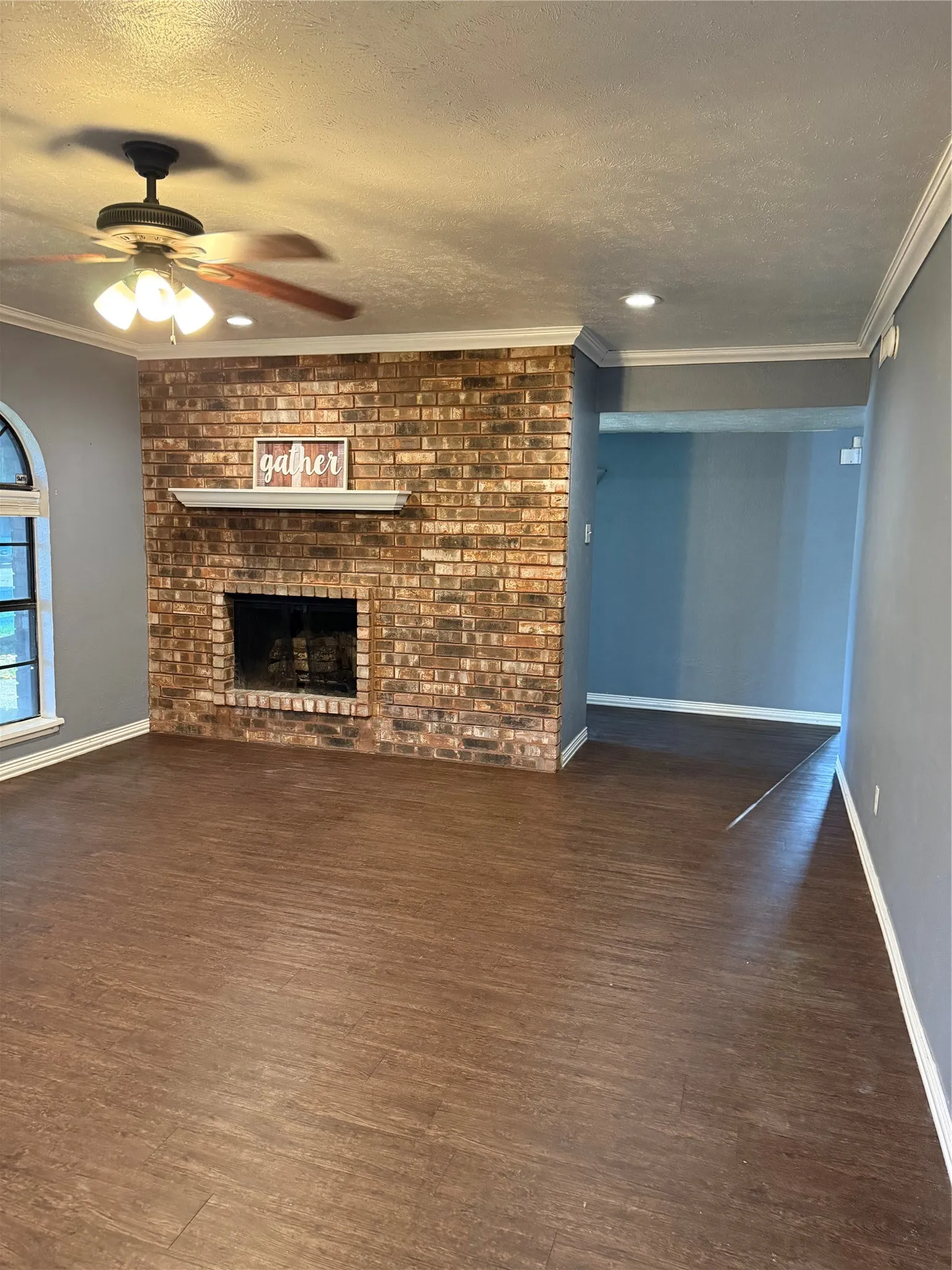 Brick fireplace with a white mantel, wood-finish flooring, recessed lighting, and crown molding