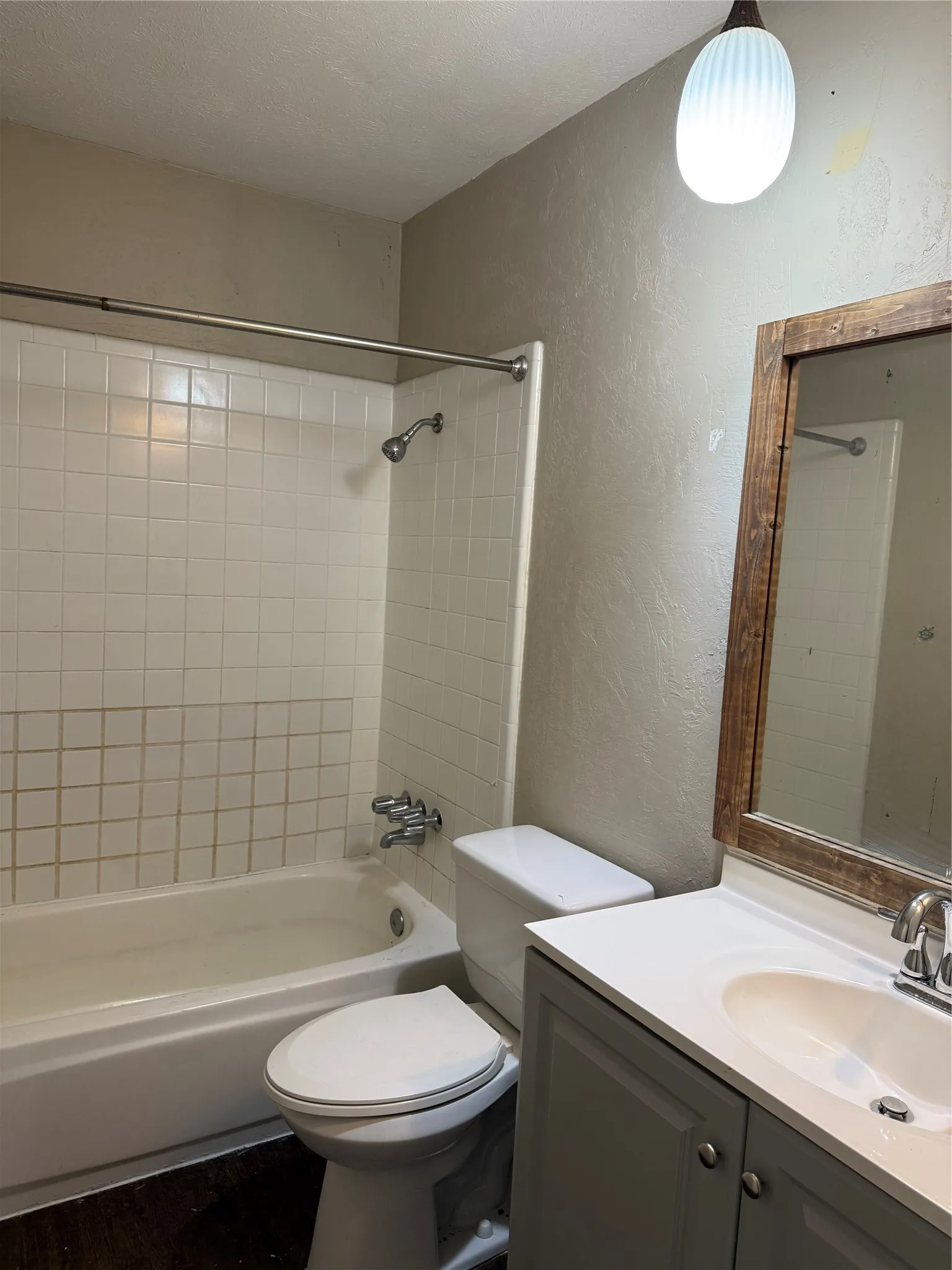 White subway tile shower surround with a built-in tub, wood-finish mirror frame, and a vanity with a white countertop and integrated sink