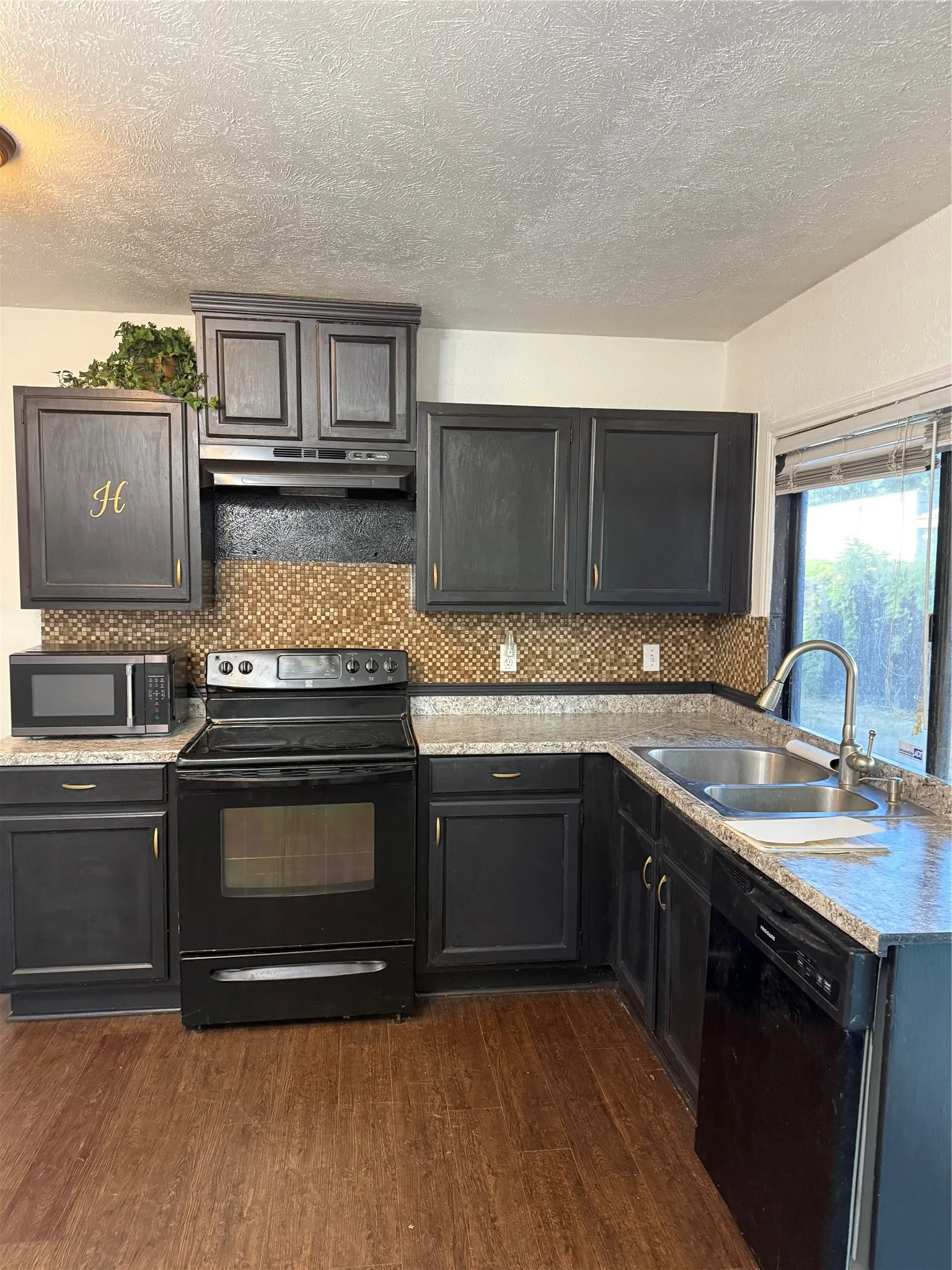 Kitchen featuring dark wood-finish cabinetry, mosaic tile backsplash, light-toned countertops, and wood-finish flooring