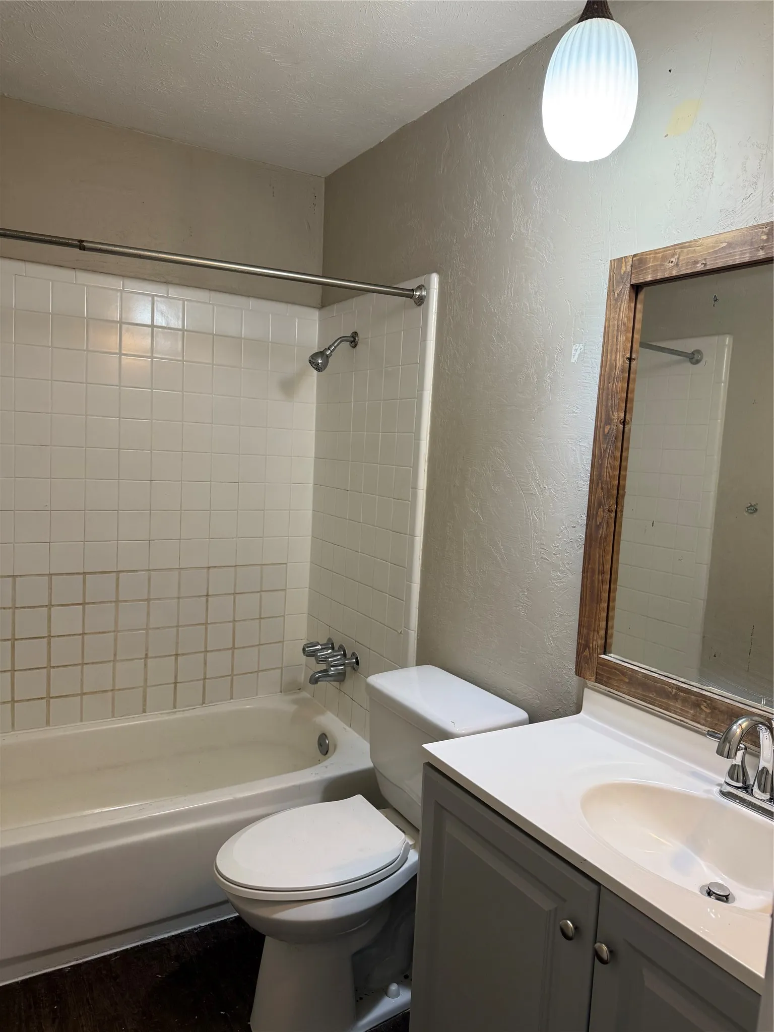 Bathroom featuring a built-in tub with tile surround, a white toilet, a vanity with a white countertop and integrated sink, and a wood-framed mirror