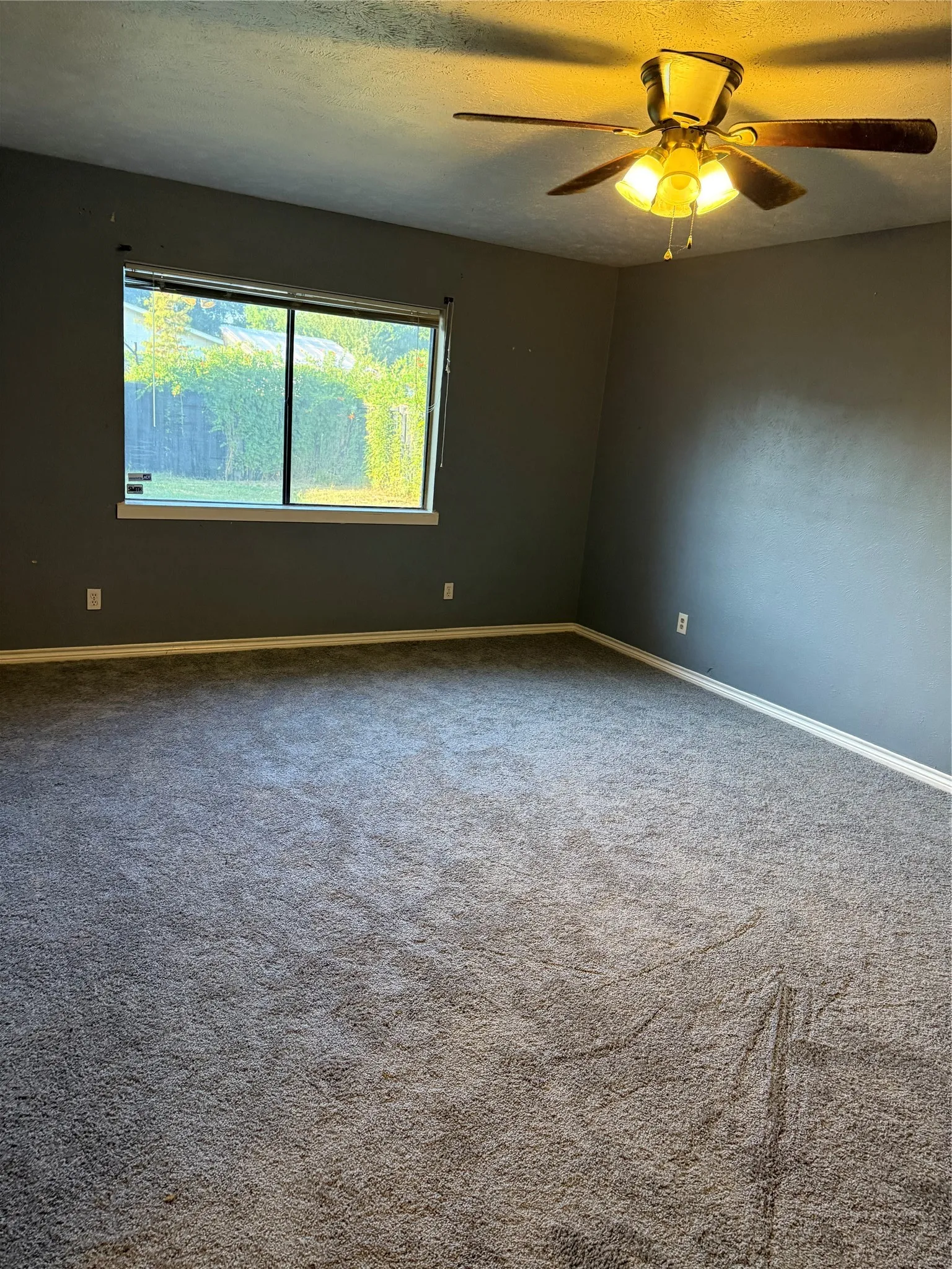 Carpeted room featuring a ceiling fan with integrated lighting, a large window, and sloped ceiling details