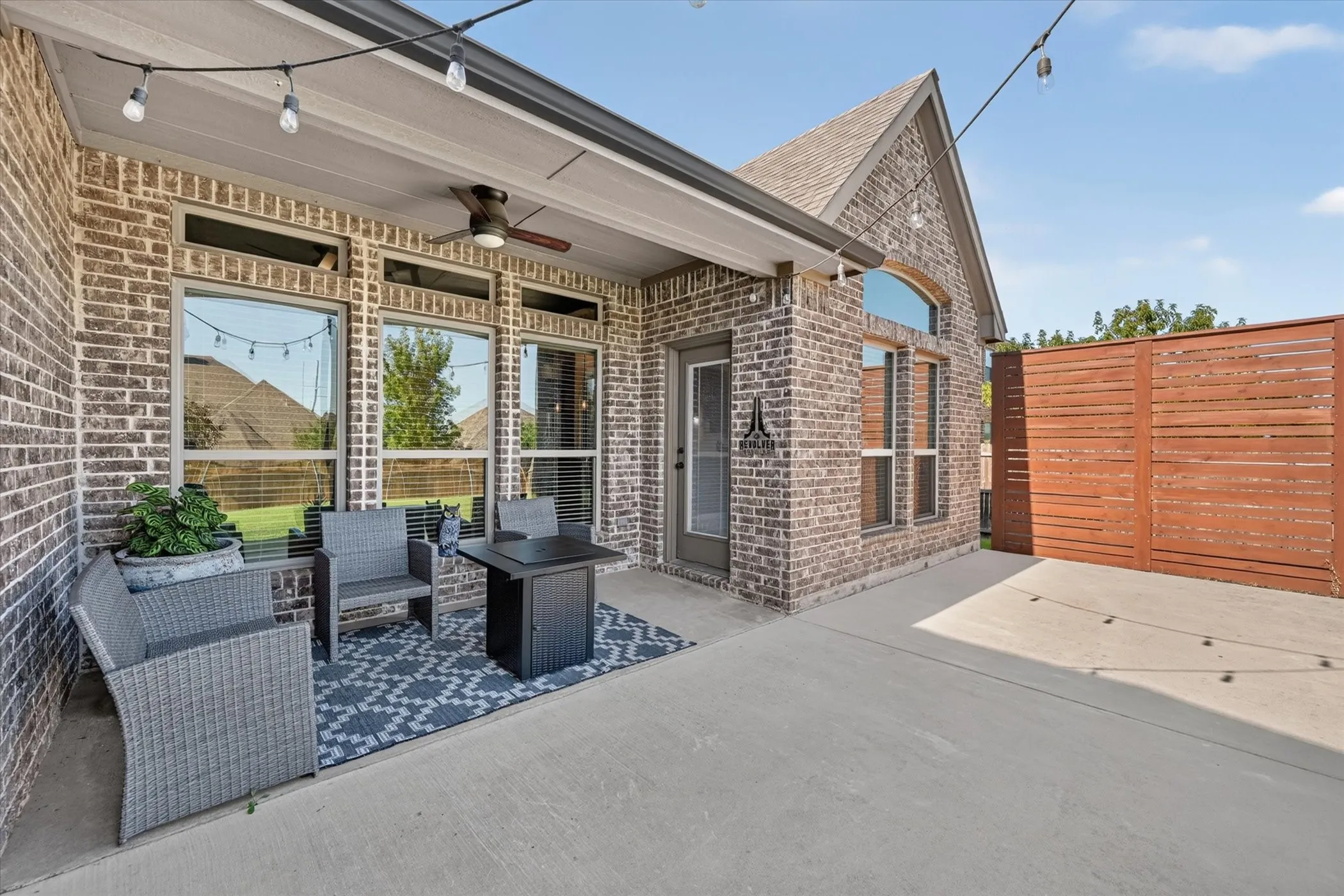 Covered patio featuring a ceiling fan, brick exterior, and wood privacy fencing