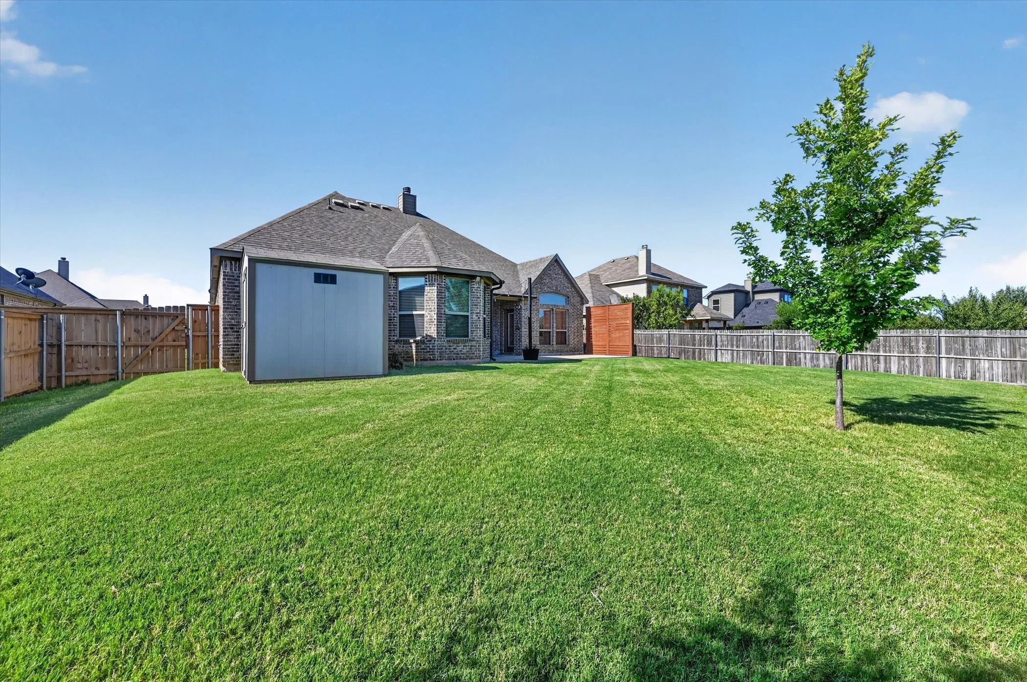 Expansive green lawn, wood privacy fencing, brick exterior, bay window, and a storage shed
