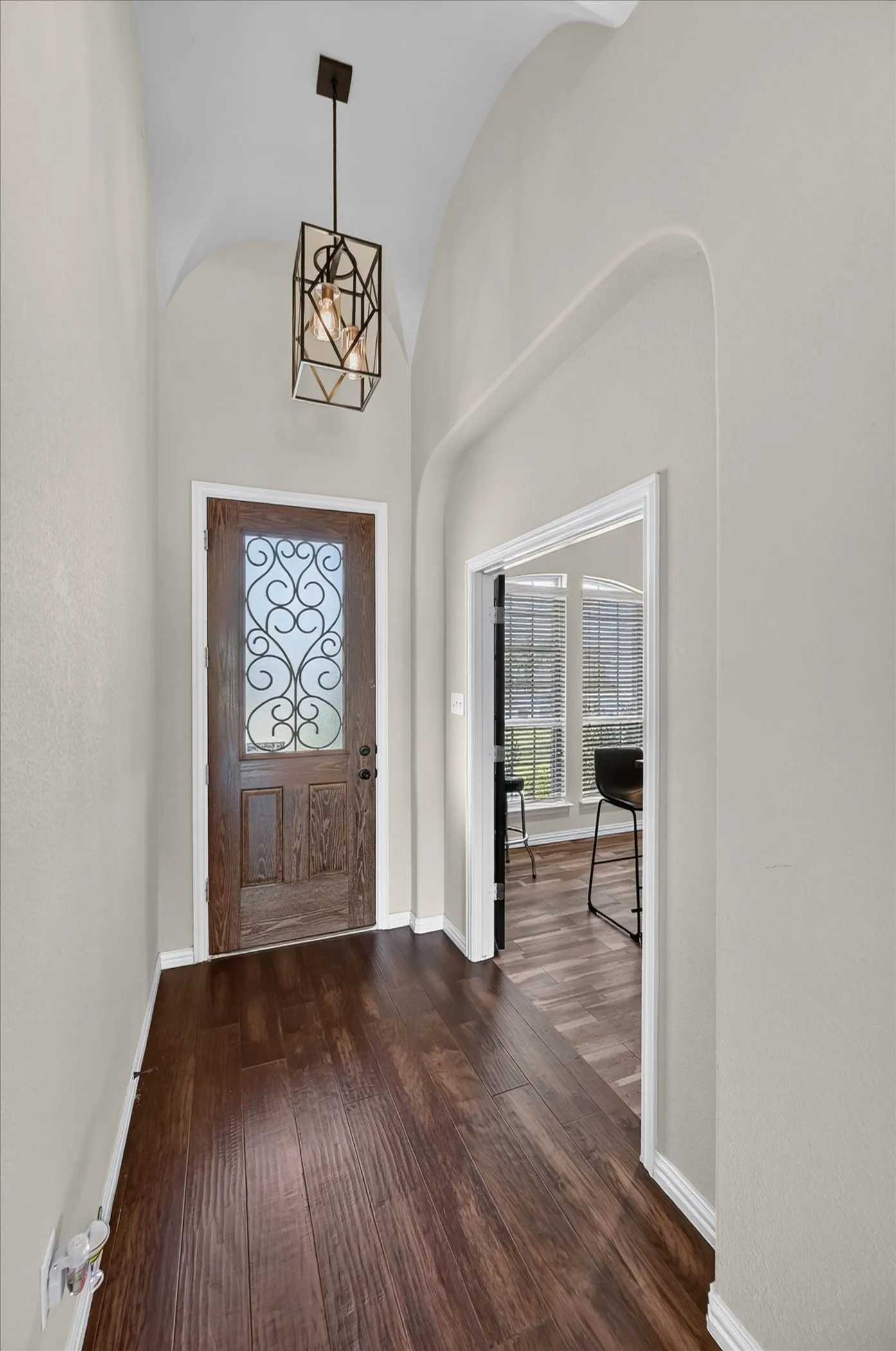 Elegant foyer showcasing soaring vaulted ceilings, rich wood-finish flooring, and architectural arches that frame the entry