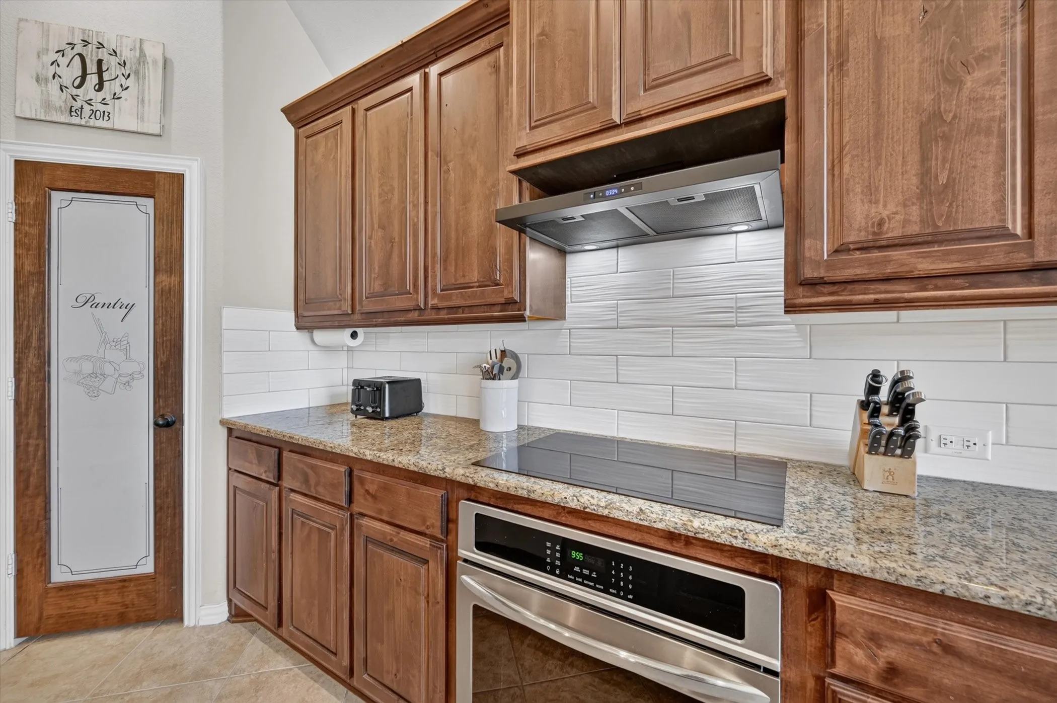 Wood cabinetry with crown molding, granite countertops, subway tile backsplash, stainless steel range hood, and built-in oven