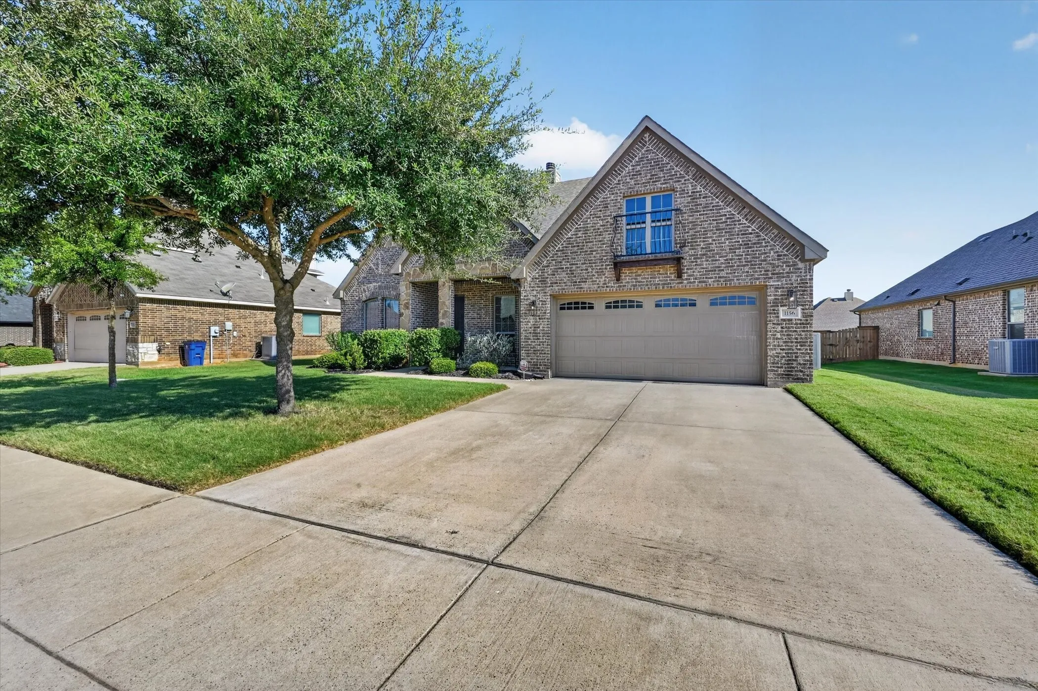 Brick Colonial home featuring a two-car garage with paneled doors, circular driveway, and mature landscaping with established trees