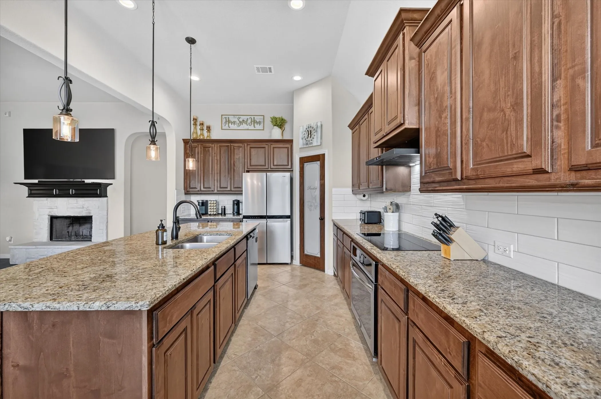 Kitchen featuring brown wood cabinetry, light granite countertops, stainless steel appliances, a white subway tile backsplash, and ceramic tile flooring