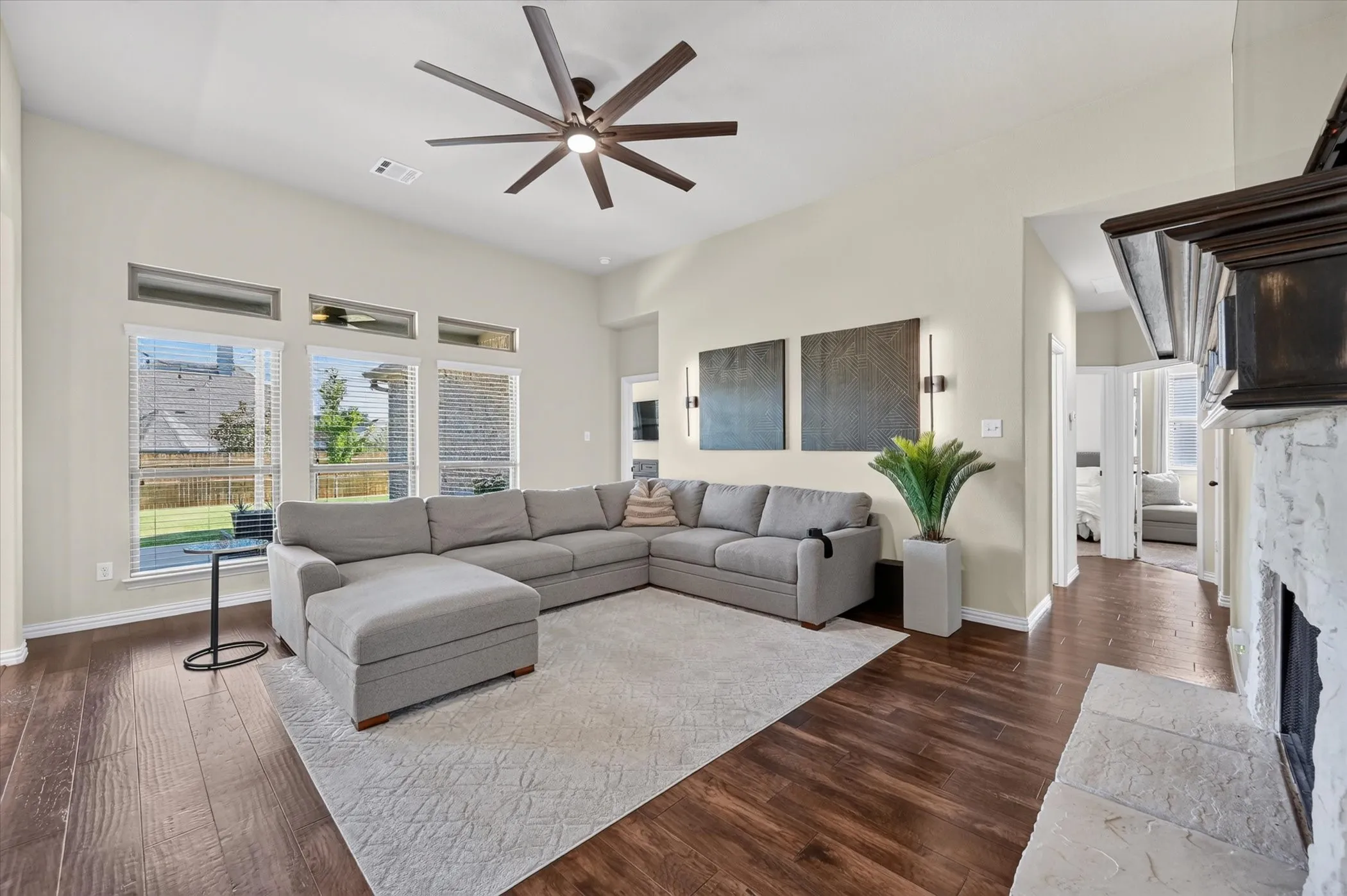 Spacious open-concept living area featuring a sectional layout with an upholstered ottoman, large-scale area rug, and modern ceiling fan