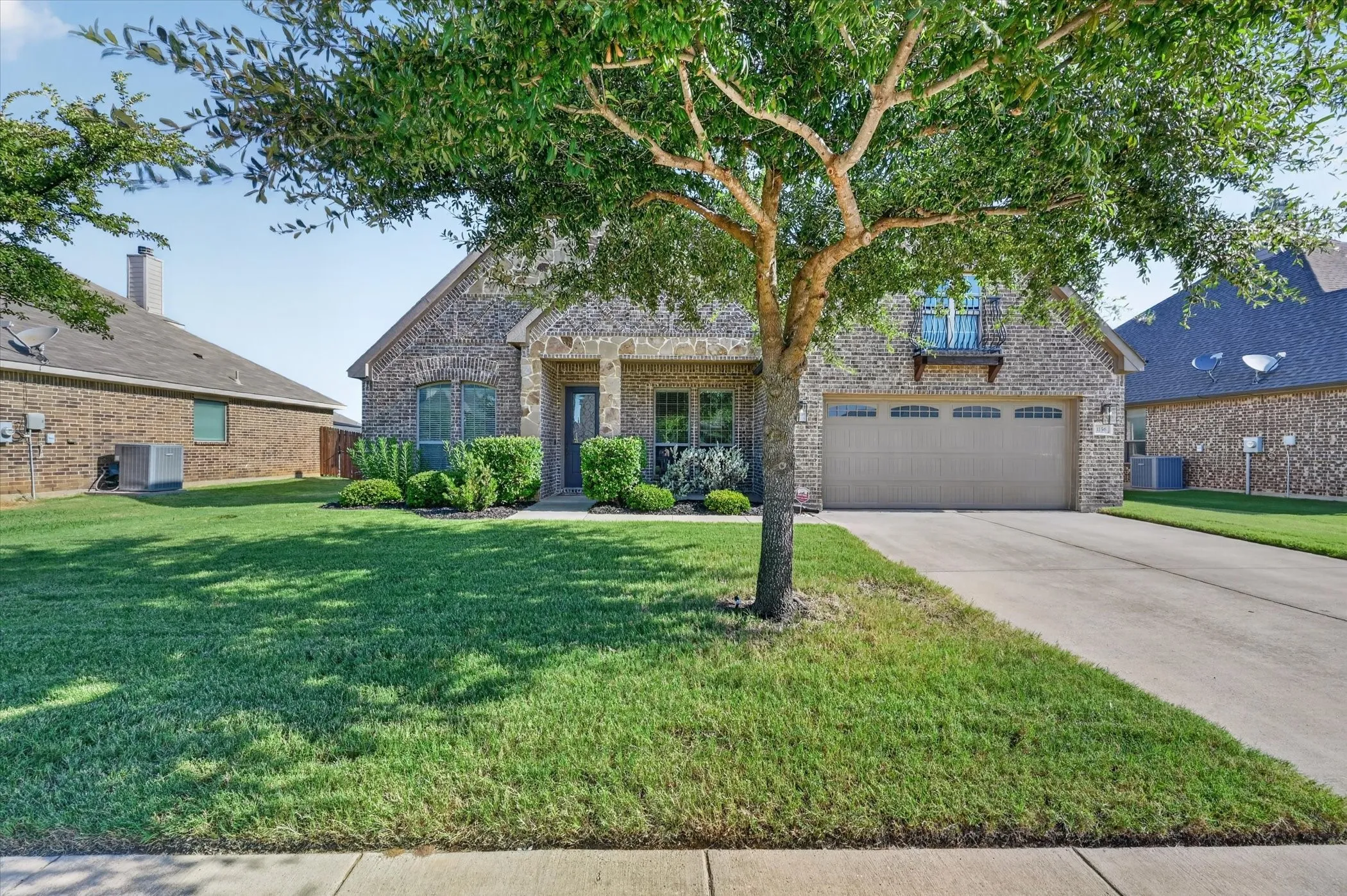 Brick exterior with stone accents, covered front entry, attached garage, and mature landscaping
