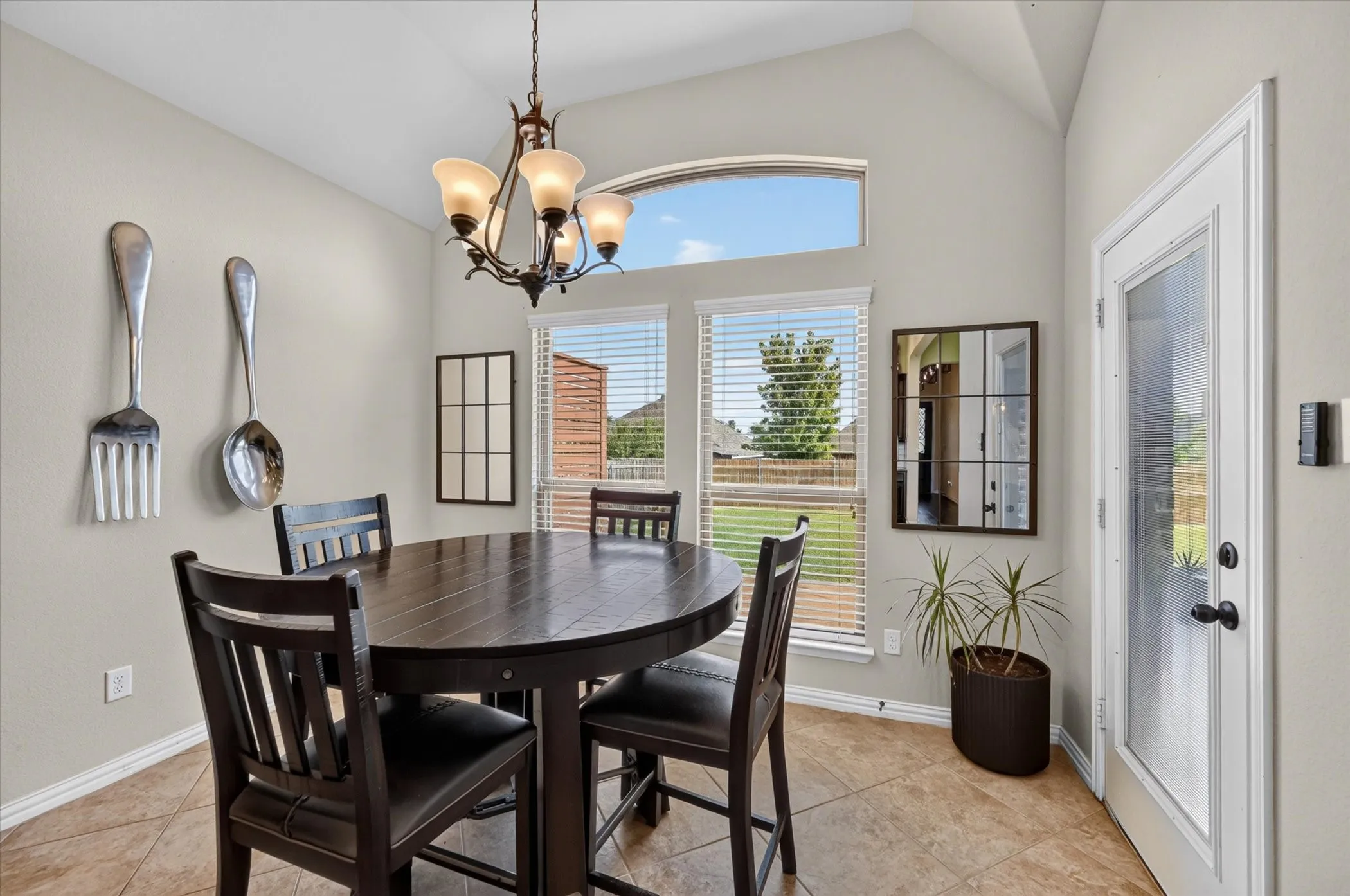 Vaulted ceiling with an arched transom window, a multi-light chandelier, tiled flooring, and a glass-paneled exterior door