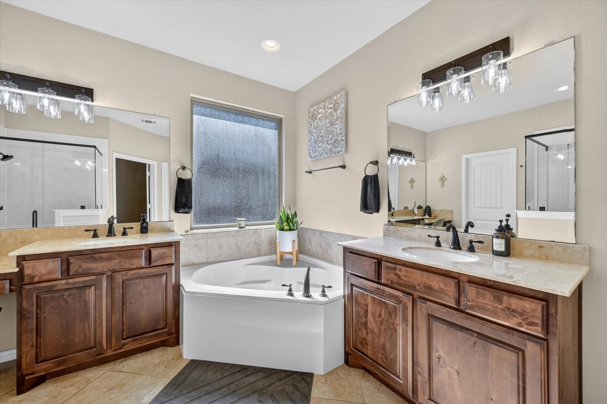 Dual wood-finish vanities with undermount sinks, corner soaking tub, large vanity mirrors, and tile flooring