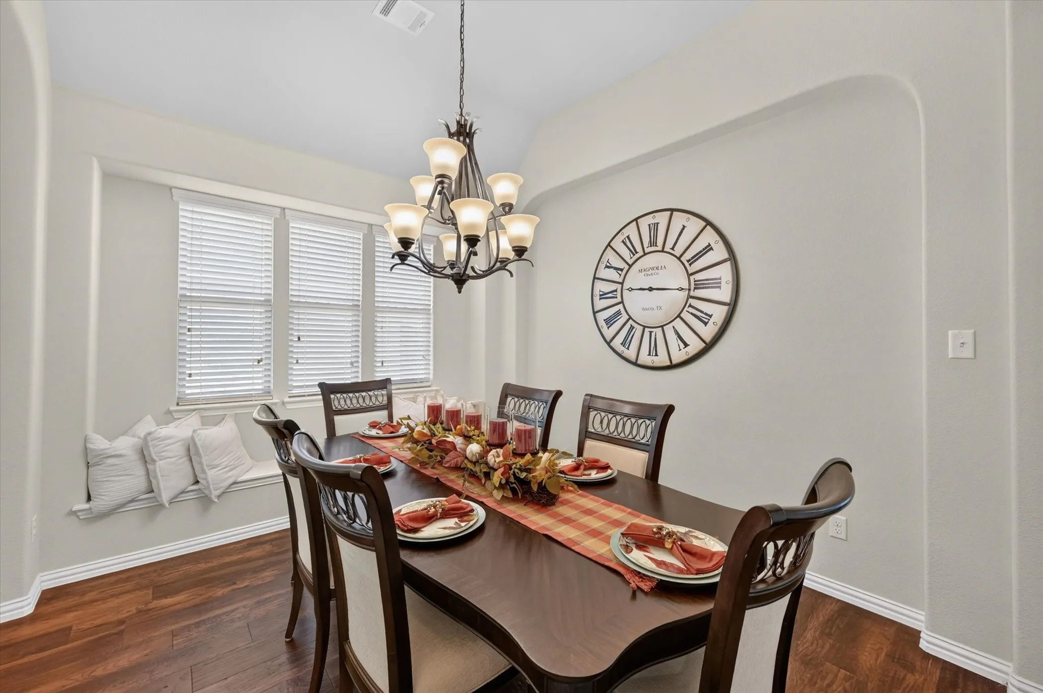 Dining area with wood-finish flooring, a built-in window seat, a multi-light chandelier, and arched wall details