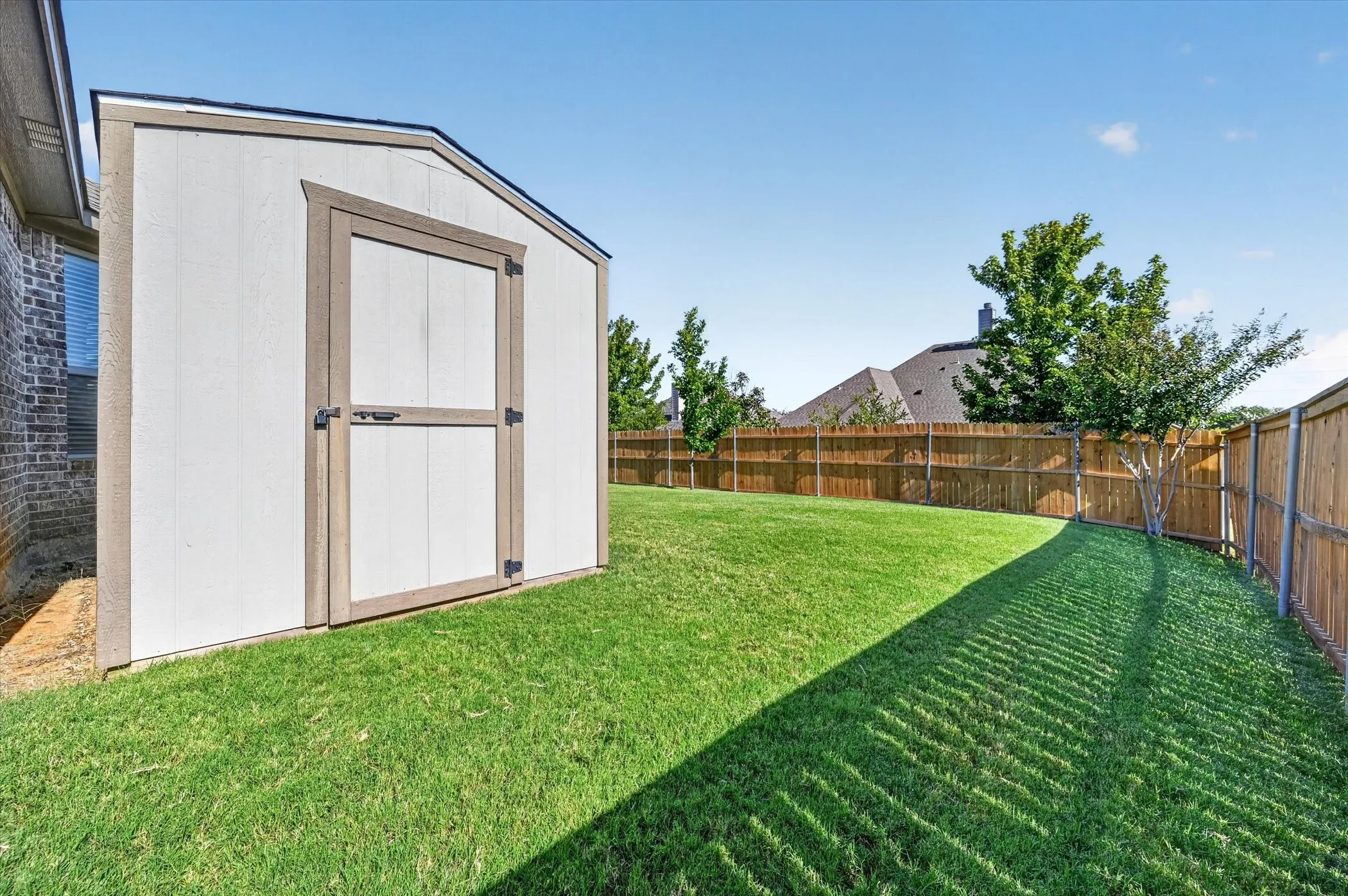 Expansive backyard featuring a newly seeded lawn, mature landscaping with mixed plantings, and wooden privacy fencing