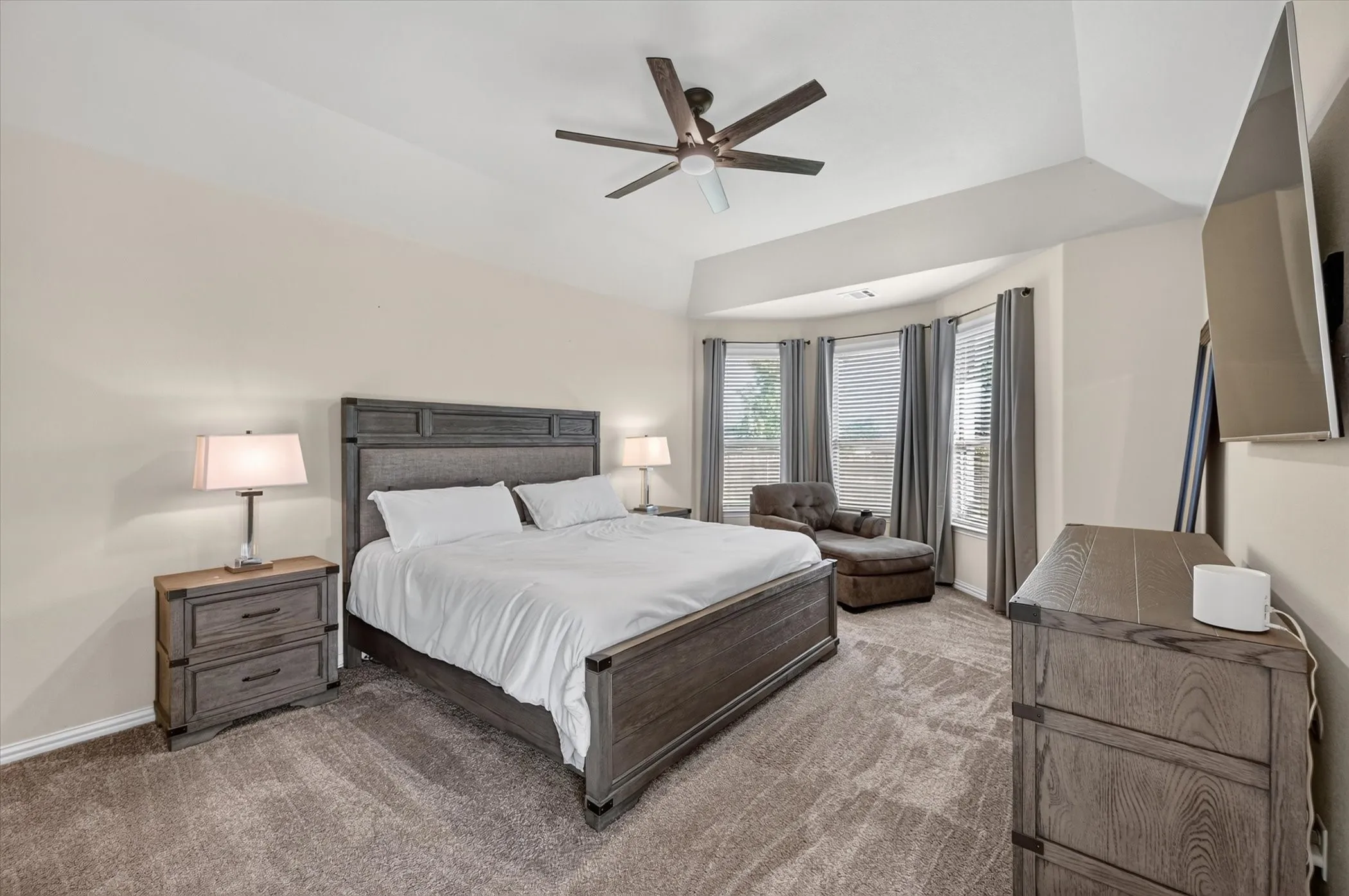 Vaulted ceiling with a ceiling fan, bay window with blinds and drapes, and neutral wall paint