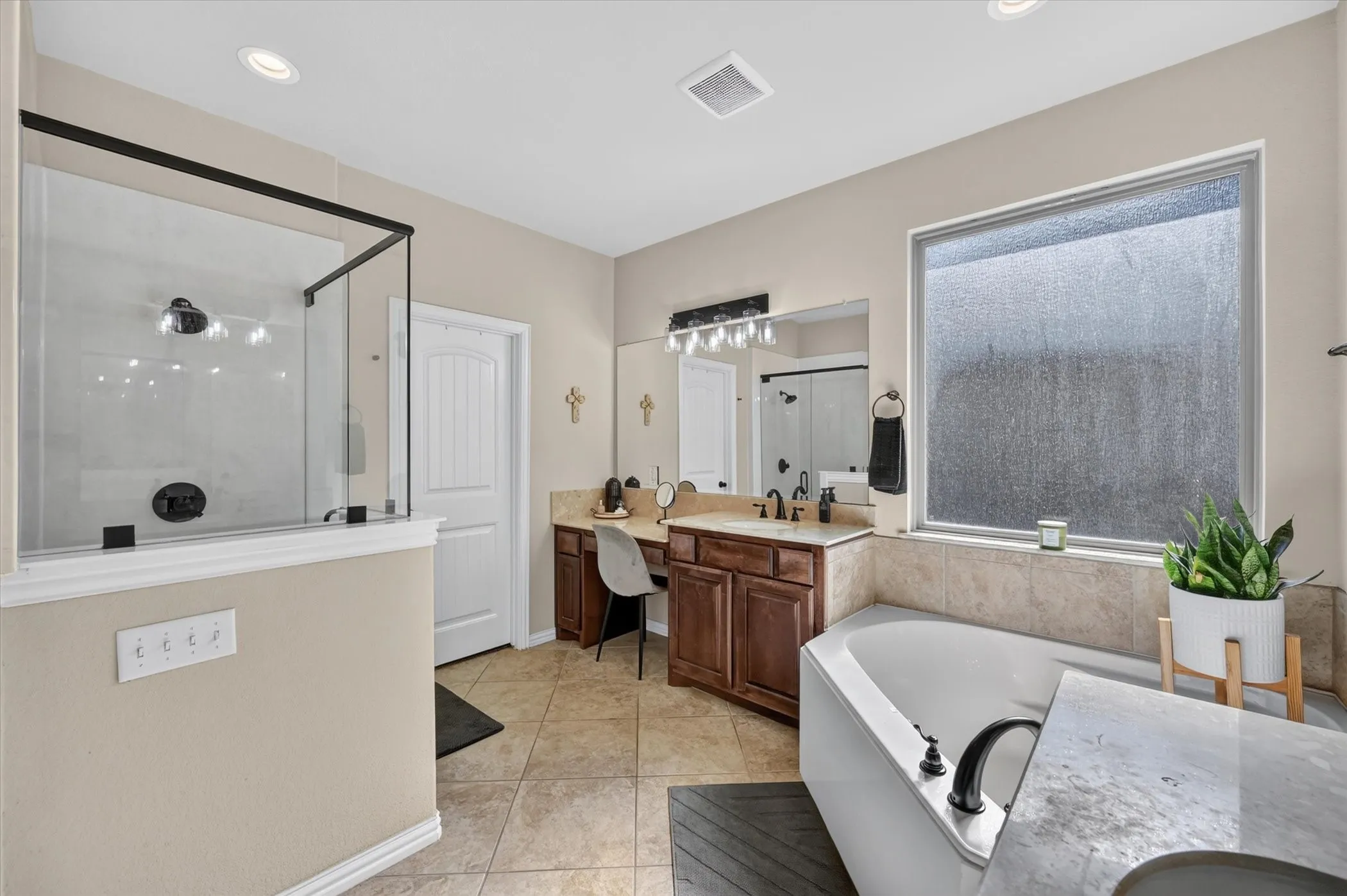 Spa-inspired primary bathroom featuring a freestanding soaking tub with integrated deck, dual-vanity with wood cabinetry and quartz countertops, walk-in shower with frameless glass enclosure and tile surround, and abundant natural light from large window